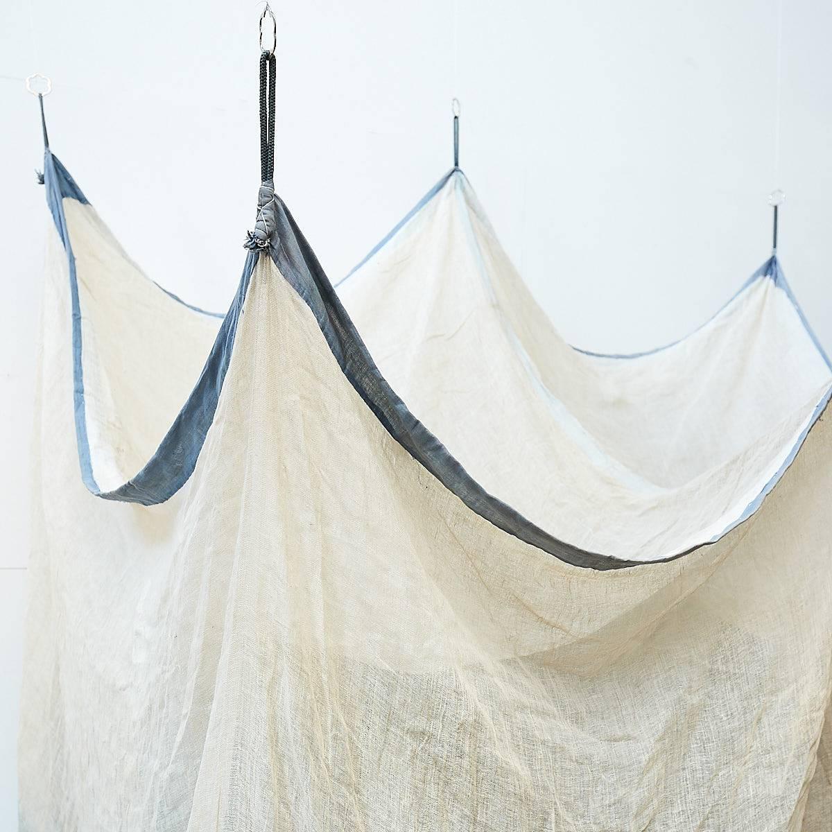 Unbleached loosely woven linen mosquito net, with hand stitching and darned patches. The linen has been dyed using natural indigo, circa 1960.