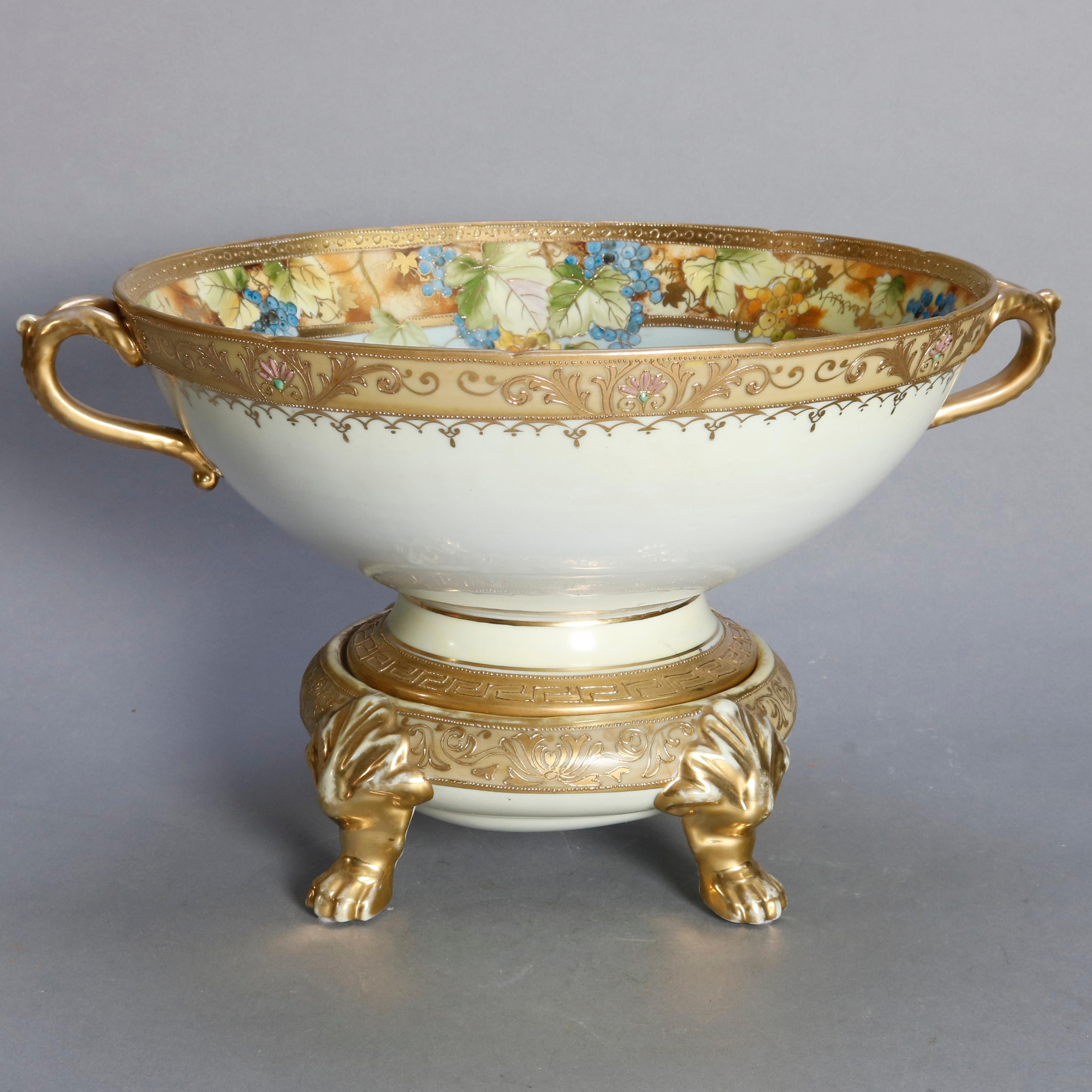An antique Japanese Nippon porcelain punch bowl offers hand painted bowl with seascape scene with sailing vessels bordered with grape and vine decoration, flanked by gilt scroll form handles and seated on gilt decorated base with paw feet, green