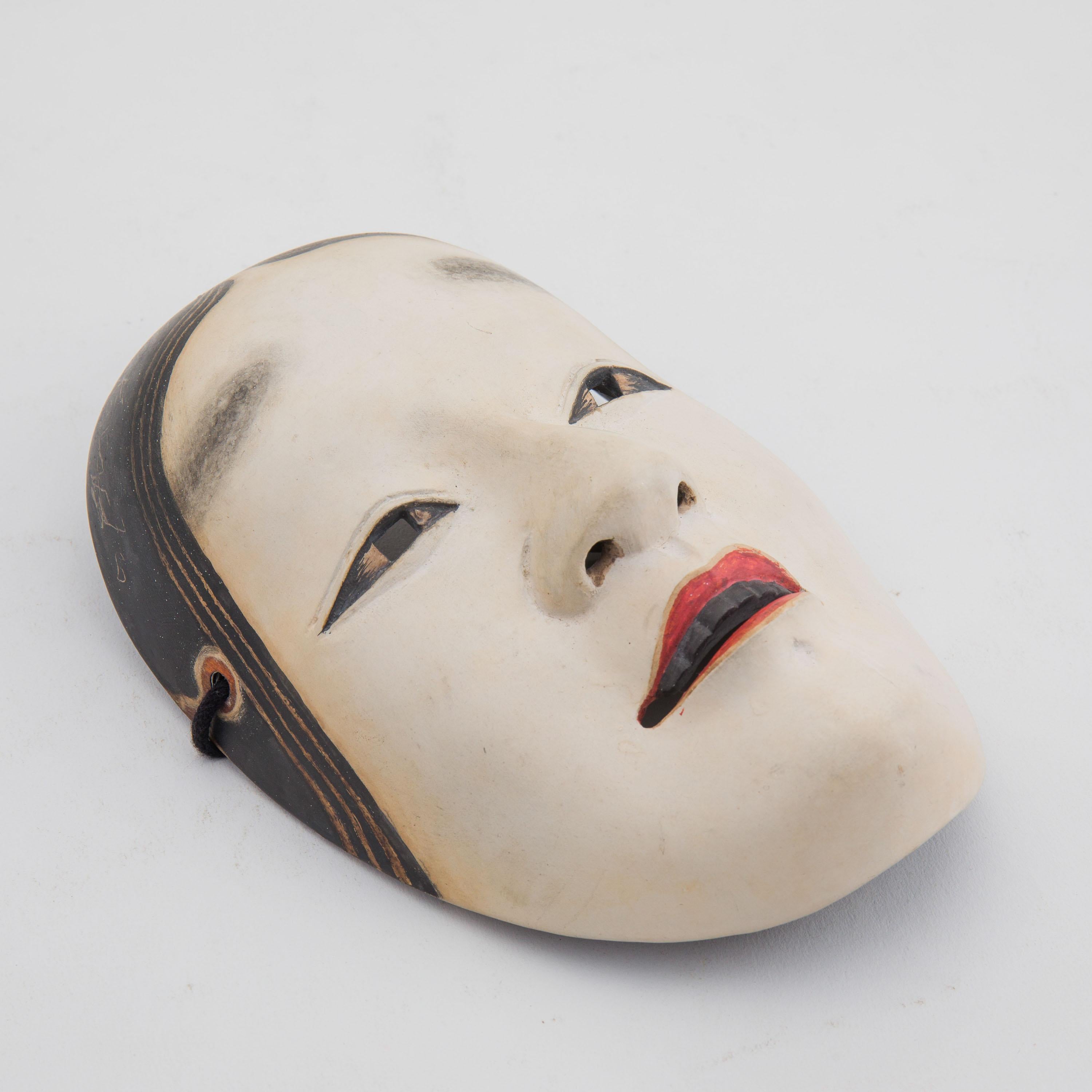 An antique hand-carved and hand-painted Japanese Noh theatre mask, depicting a young female character (onna men). Noh masks have been described as being like 