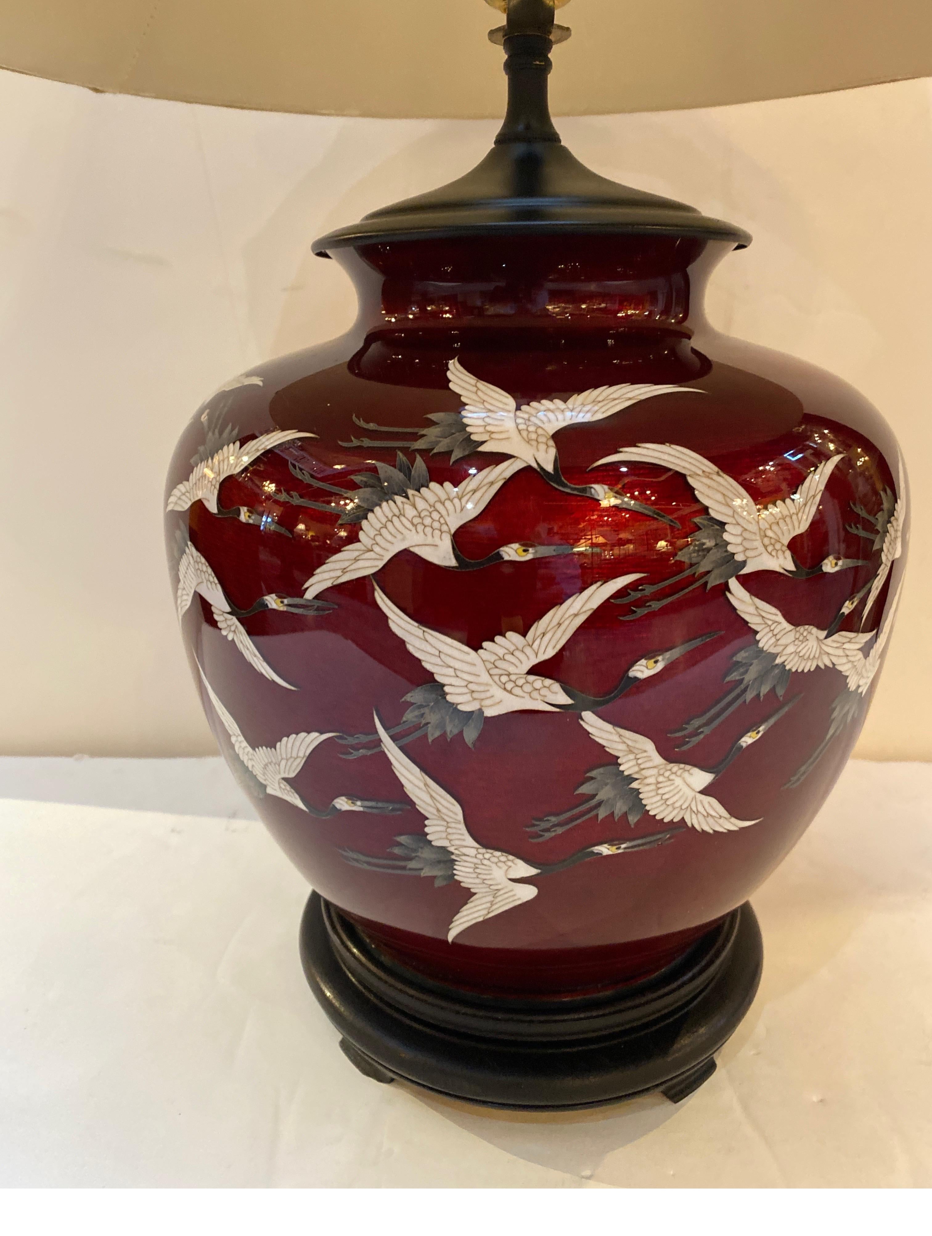 A Japanese cloisonné vase now electrified. The 1920's pigeon blood red background with a flock of white flying cranes as decoration. The matt black cap with a black wood Asian style base. The shade is for photographic purposes only and not included.