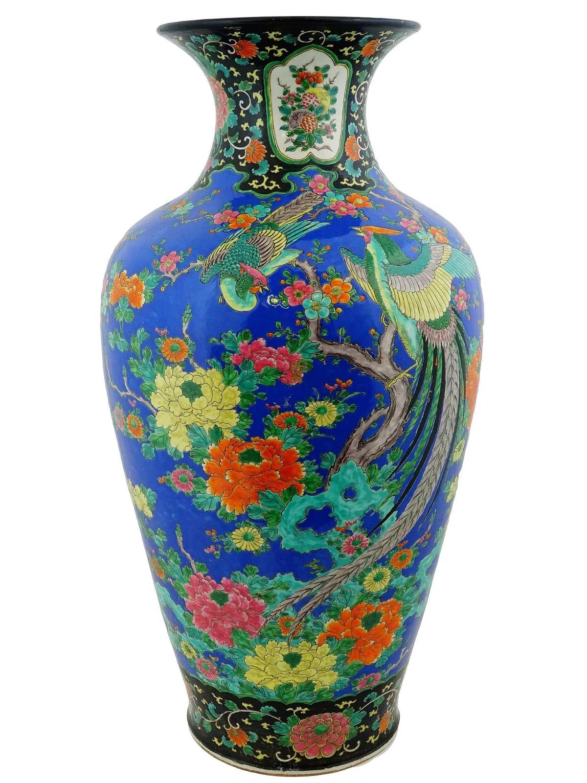 An antique Japanese porcelain vase. The vase is hand enameled with a vibrant blue background and is decorated with colorful images of birds perched on branches amidst flowering plants, including peonies and other blossoms. The vase has a baluster
