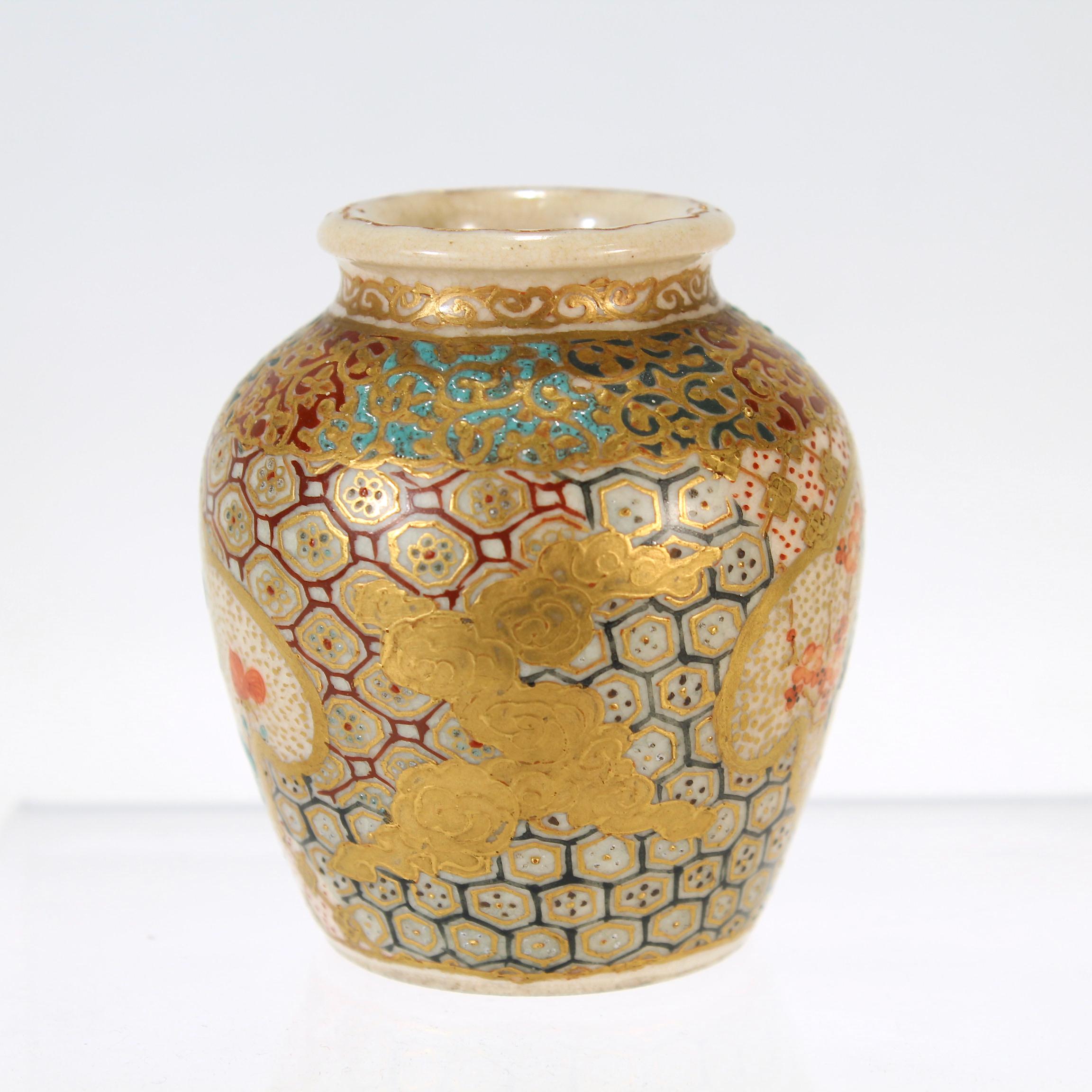 Eine feine, winzige, antike japanische Satsuma-Keramik-Vase.

Durchgehend mit Vergoldung und erhabener Emaille verziert.

Auf der Vase befinden sich zwei Kartuschen, die mit roten Blumen (möglicherweise Pfingstrosen) und Vögeln verziert