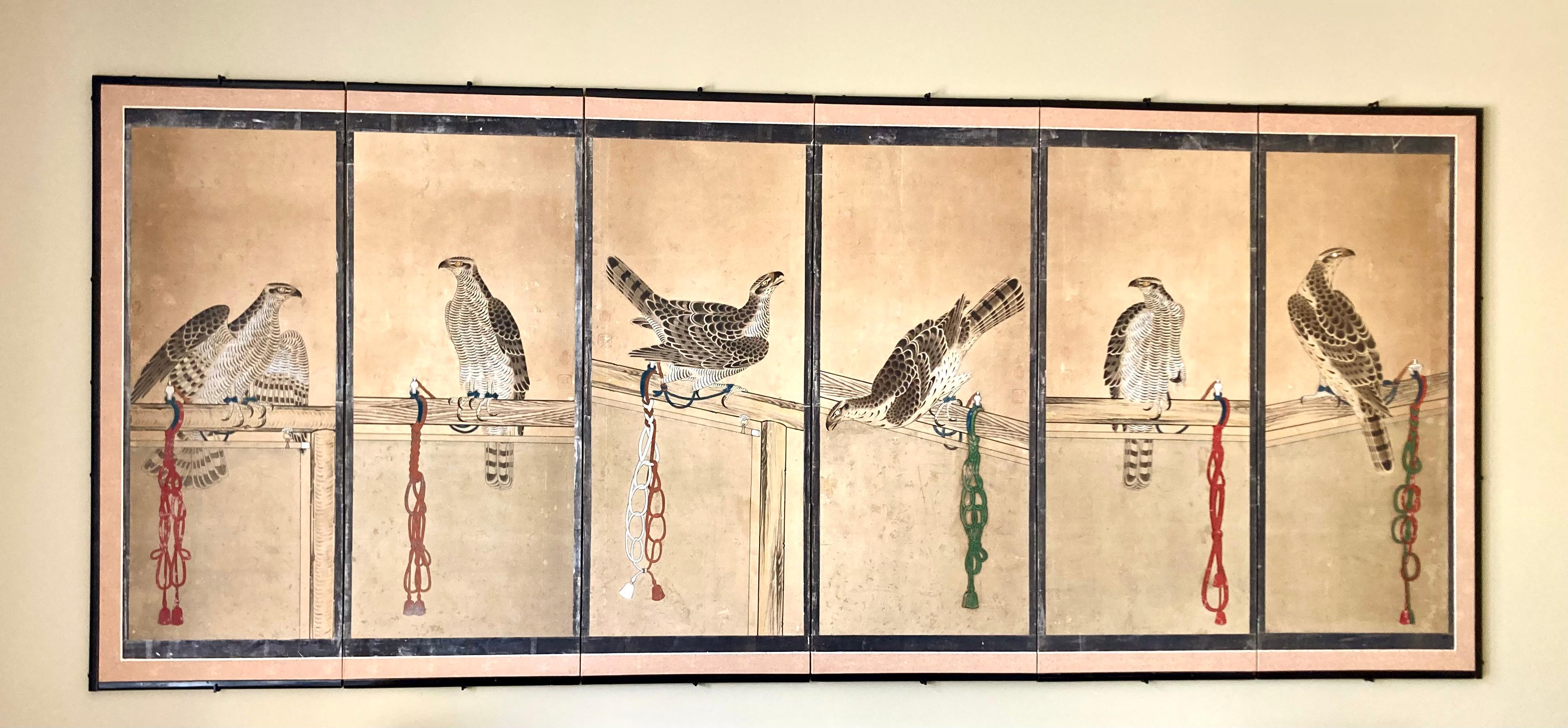 A striking Japanese antique Edo period screen painting in ink and colors on paper, each of the 6 framed panels featuring a goshawk (hawk) tethered to a perch by a silk cord with the distinctive knots of various samurai clans, with silver leaf