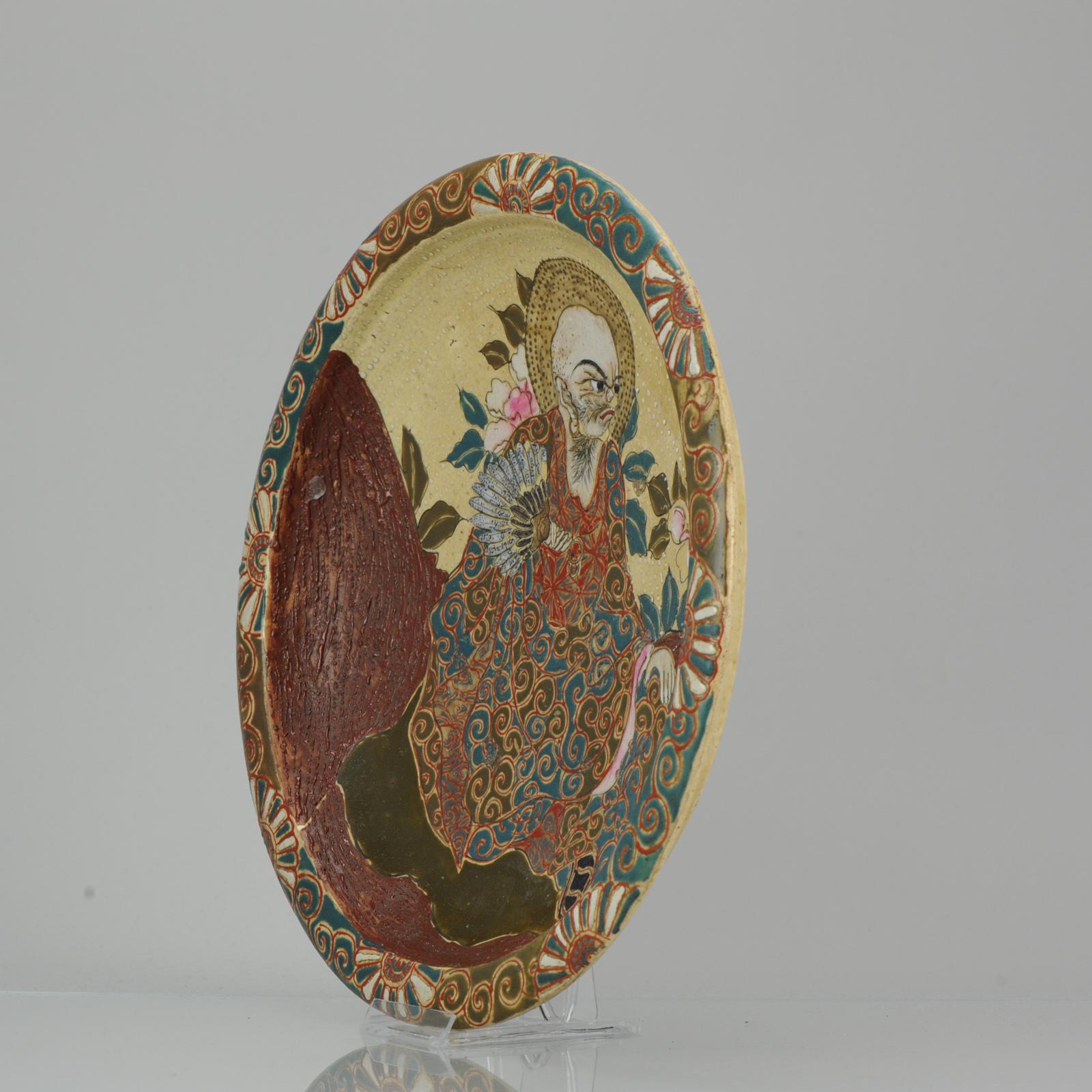 This Fabulous Japanese Satsuma Style Earthenware Charger. With a central scene of what we think is an Arhat. He is carrying a fan in his hand and behin his head a halo is visible. Check the facial expression on the mans face Large part of the piece