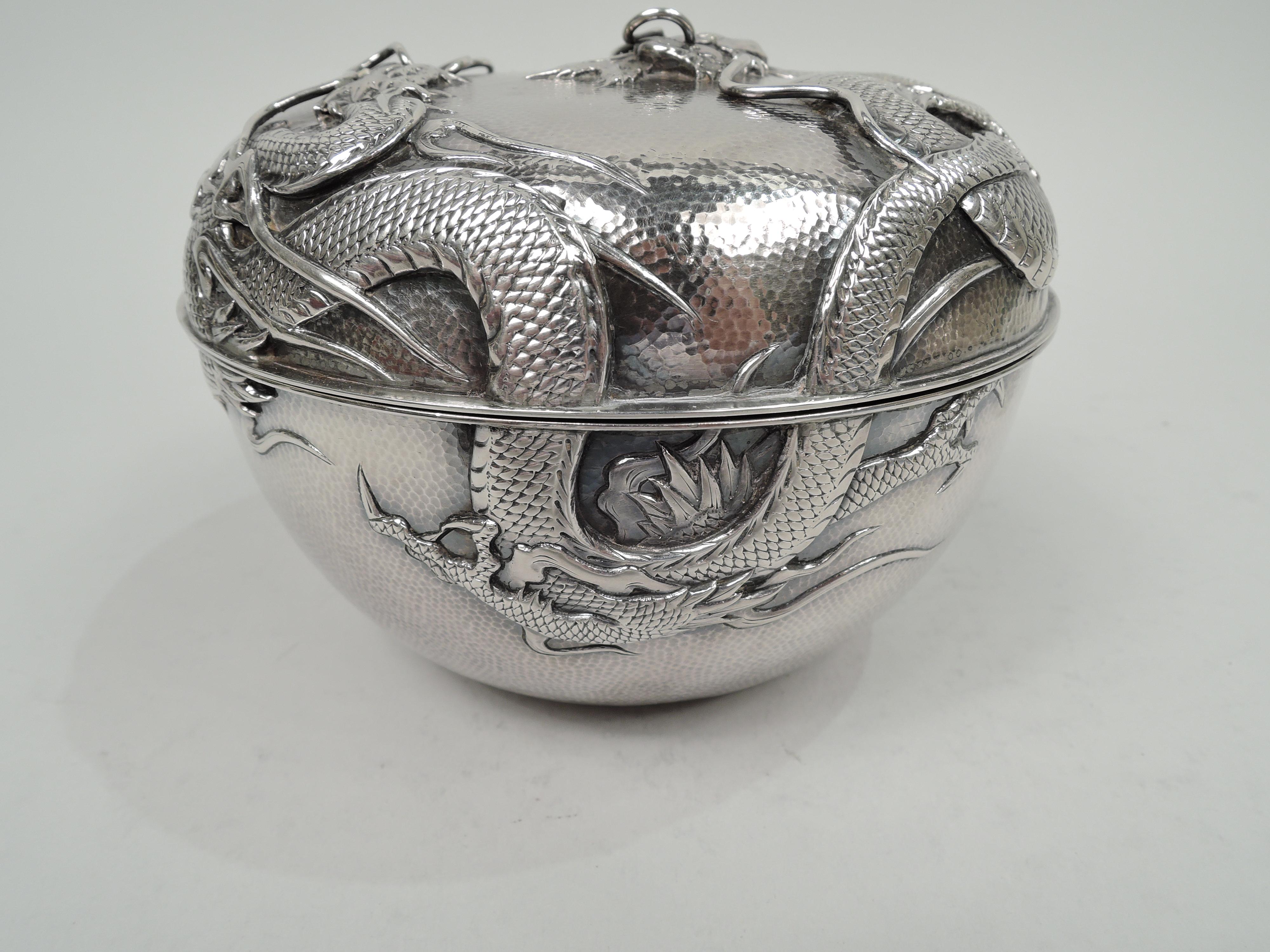 Turn-of-the-century Japanese silver dragon box. Round with curved sides and raised cover. On spot-hammered ground are applied two scaly beasts with sharp talons and spiked backs slithering around sides with horned and whiskered heads meeting on