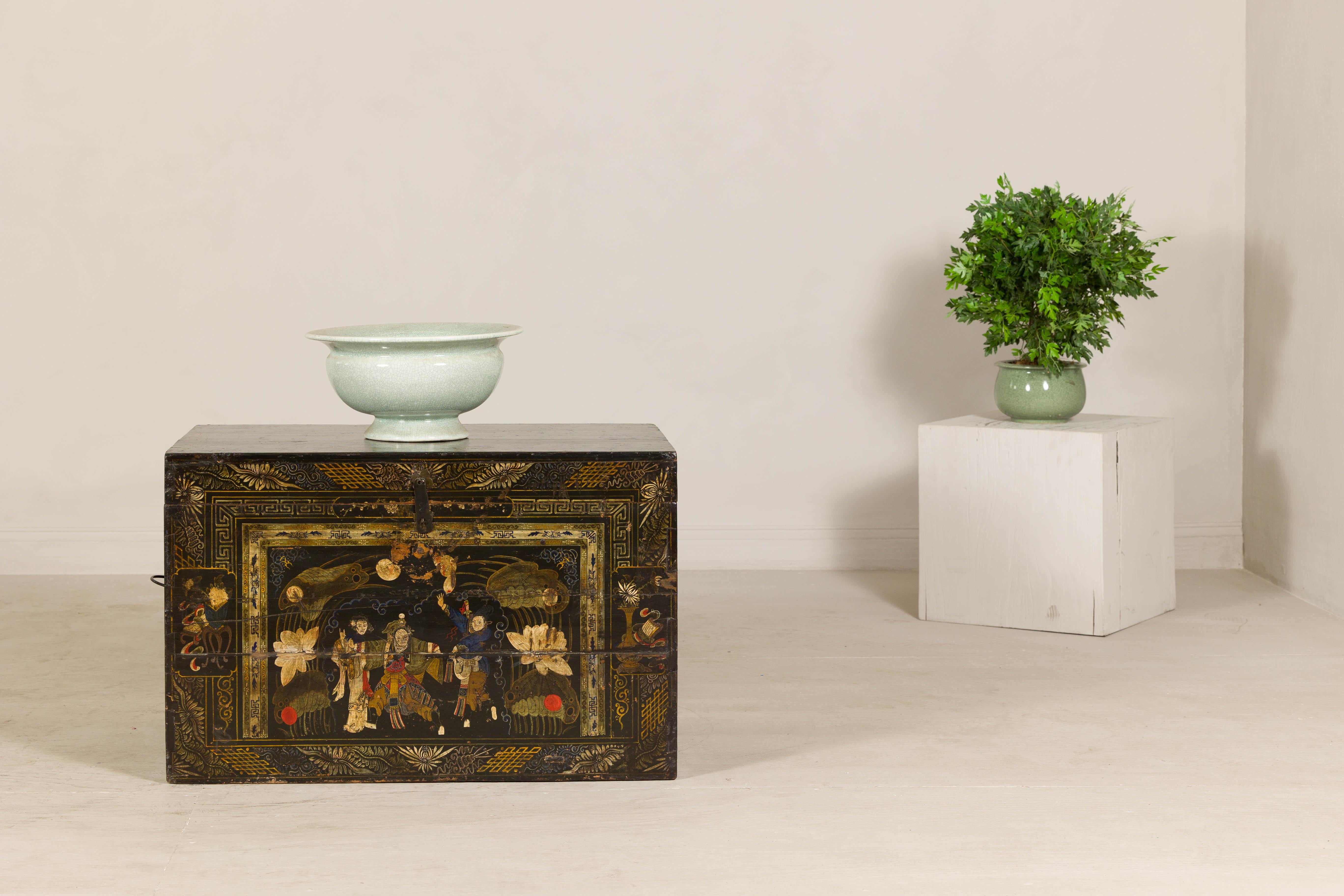 Cette malle chinoise du début du XXe siècle, datant de la fin de la dynastie Qing, séduit par son décor complexe peint à la main et sa riche finition laquée. D'inspiration japonaise, le panneau frontal présente un tableau de personnages au milieu