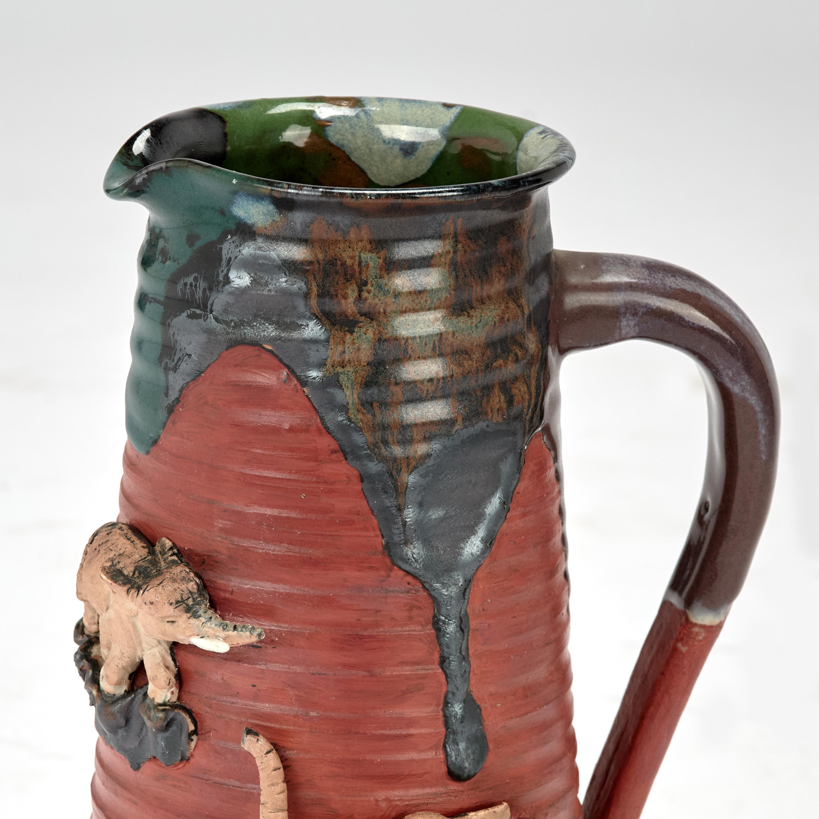 Superbe pichet ancien en poterie japonaise fabriqué à la main selon la technique traditionnelle Sumida Gawa, avec un glaçage goutte à goutte sur des éléphants formés à la main sur un fond rouge. 