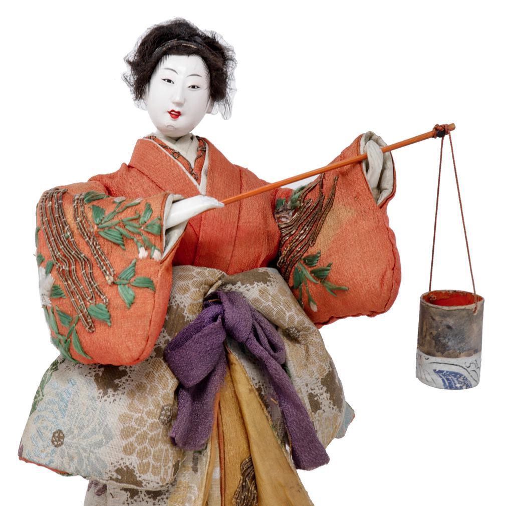 Antique Japanese Takeda Ningyo, depicting Murasame carrying a shiokumi (salt brine bucket) suspended on the end of a pole, dressed in layered kimono, the top layer arms withdrawn revealing the long crepe silk chirimen sleeves underneath, embroidered