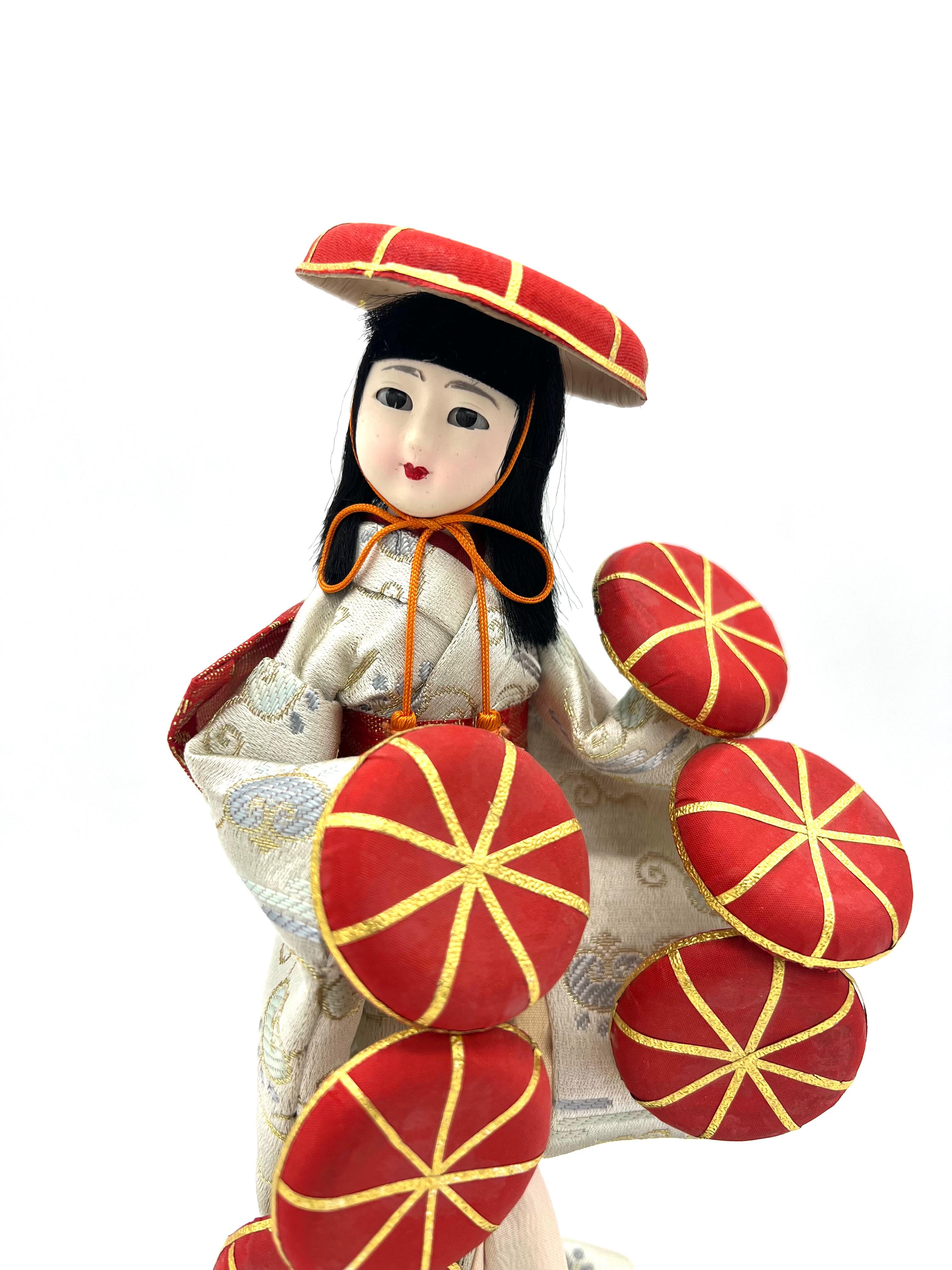 Il s'agit d'une poupée de danse traditionnelle Temari fabriquée à la main dans les années 1990.

Le site  La poupée représente un interprète de la danse traditionnelle Temari (handball). 
Elle est vêtue d'un kimono de brocart ivoire aux délicats