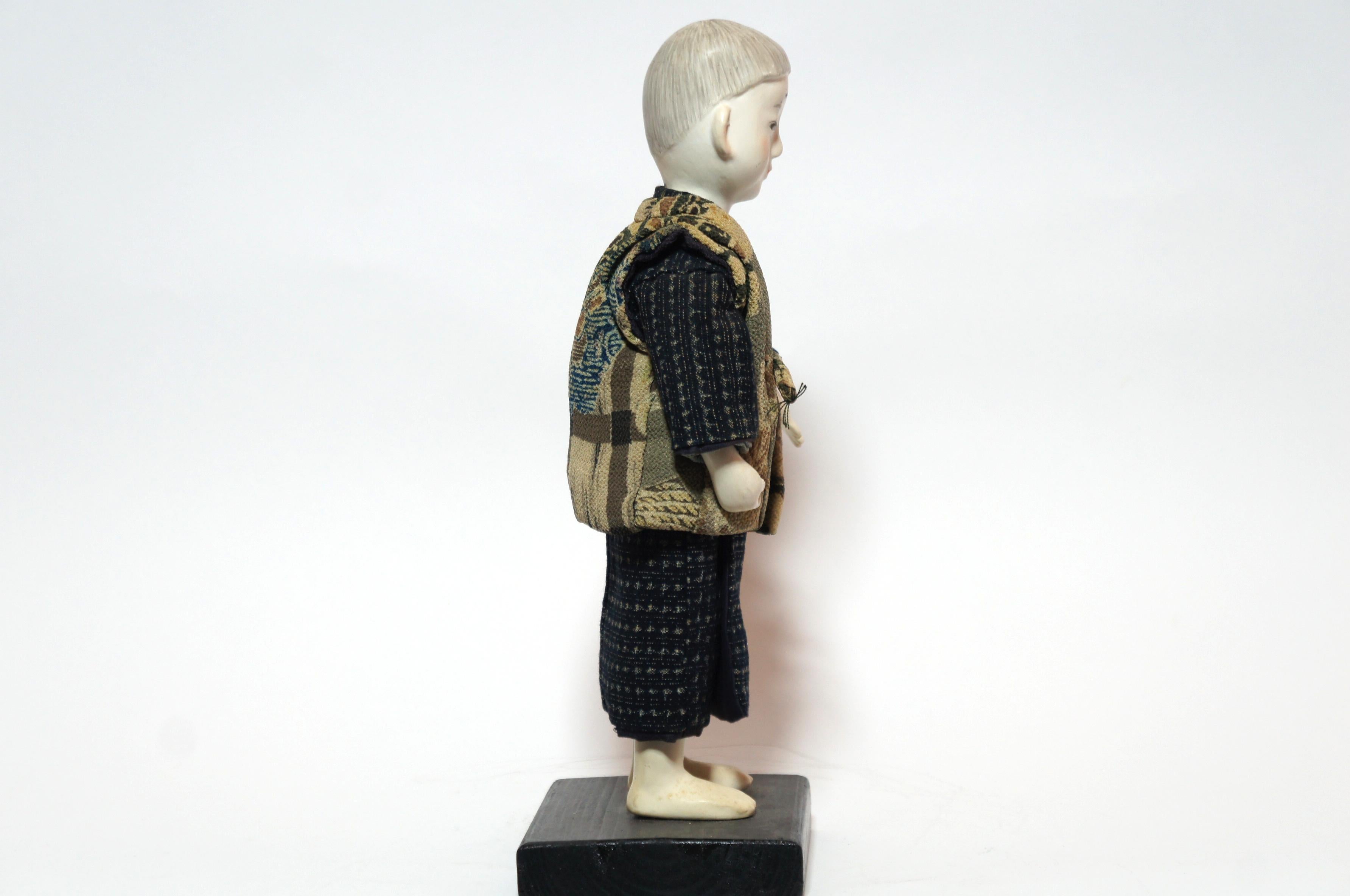 This is a traditional Japanese doll with kimono called 'Kimekomi ningyo', made in Taisho era around 1912-1926s.
Kimekomi dolls are made of woods. The clothes are glued or forced into a slot in the base of the doll. 
Some of kimekomi dolls like