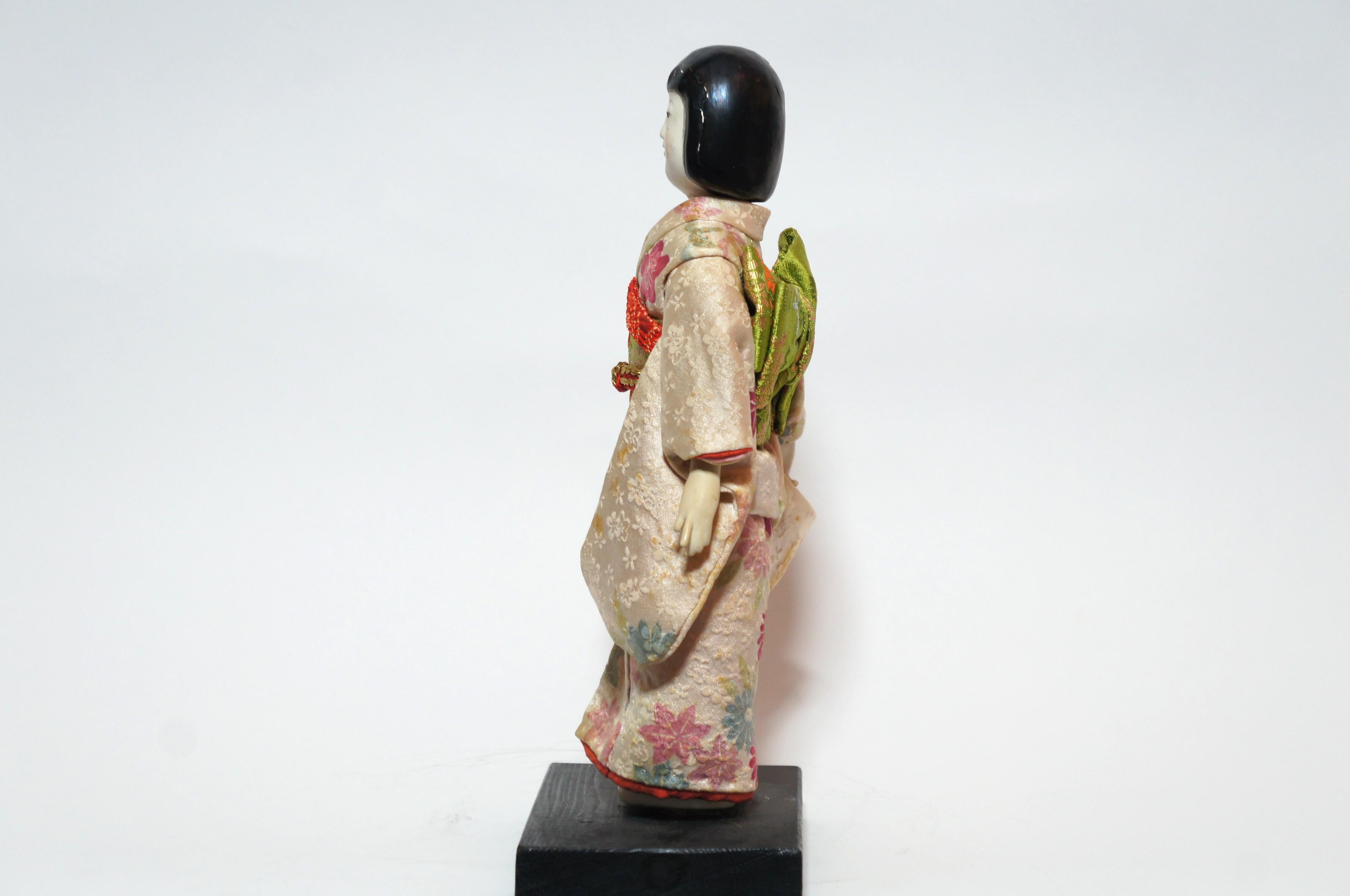 Dies ist eine traditionelle japanische Puppe mit Kimono namens 'Kimekomi ningyo', hergestellt in der Taisho-Ära um 1912-1926.
Kimekomi-Puppen sind aus Holz gefertigt. Die Kleidung wird in einen Schlitz im Sockel der Puppe geklebt oder gedrückt.