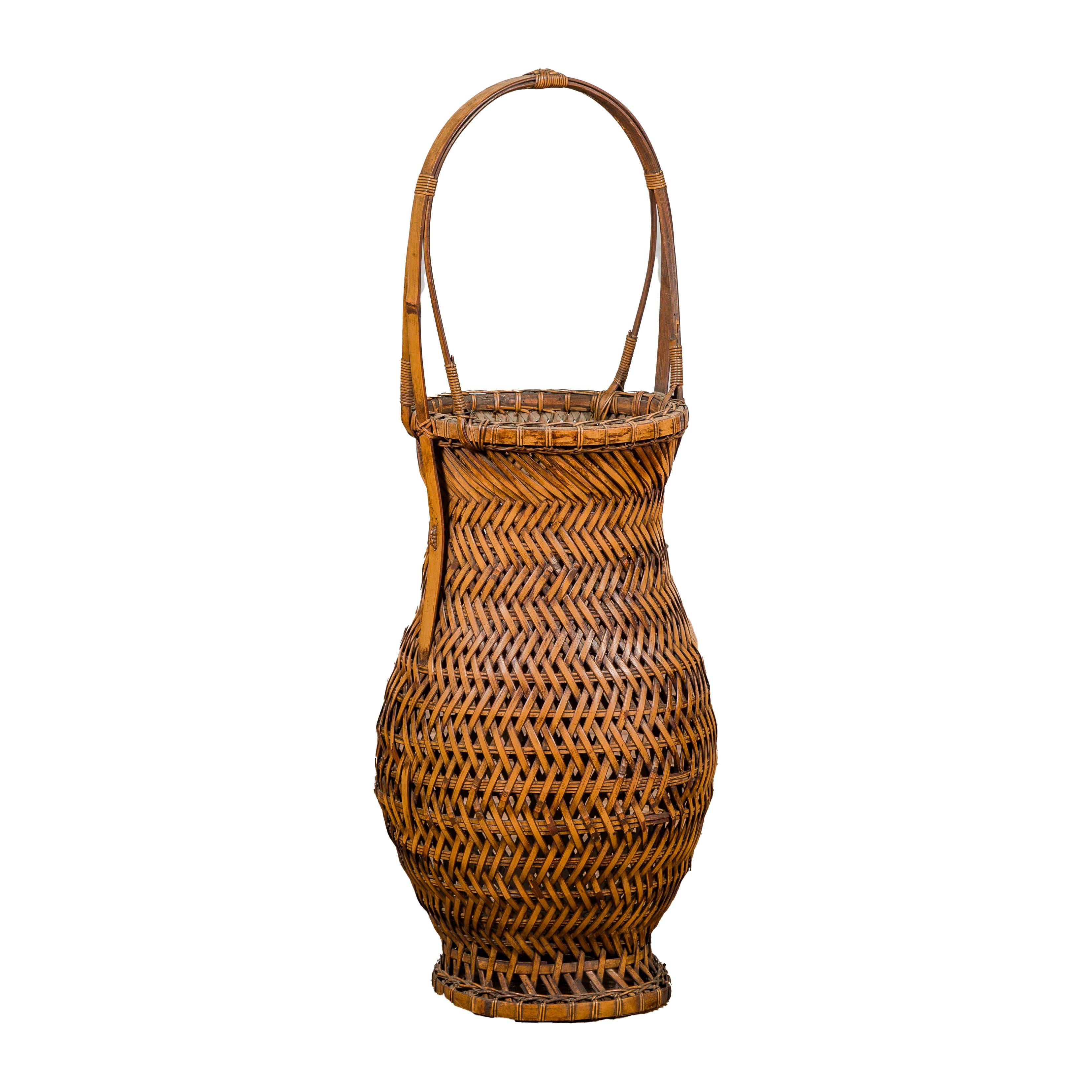 An antique Japanese woven bamboo Ikebana basket from circa 1900 with generous rounded silhouette and large handle at the top. This antique Japanese woven bamboo Ikebana basket, hailing from circa 1900, is a splendid example of traditional Japanese