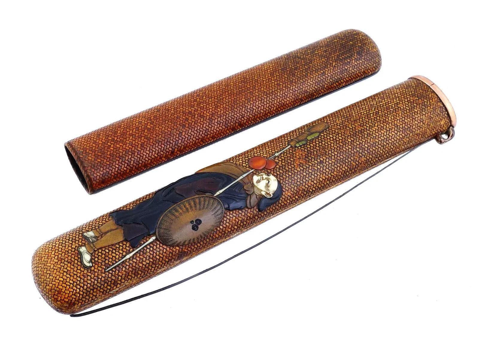 An antique Japanese woven rattan kiseruzutsu, or pipe case, inlaid with a detailed warrior image crafted from wood and natural materials. The piece is accompanied by a cord and features a signature in seals form on inlaid tablets. Circa the early