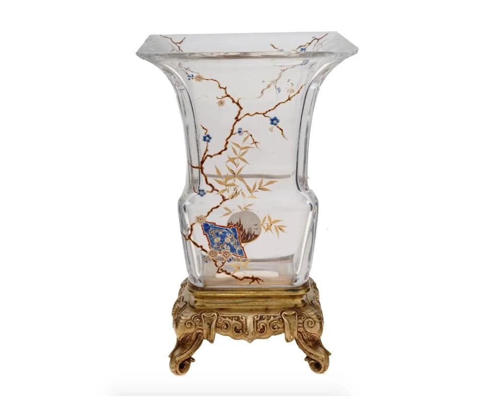 An antique French Baccarat glass vase with a fluted mouth. The vase is adorned with hand painted floral and foliage motifs in the Asian manner, decorated with gilding. Completed with a footed gilded bronze stand. The legs are made in a shape of a
