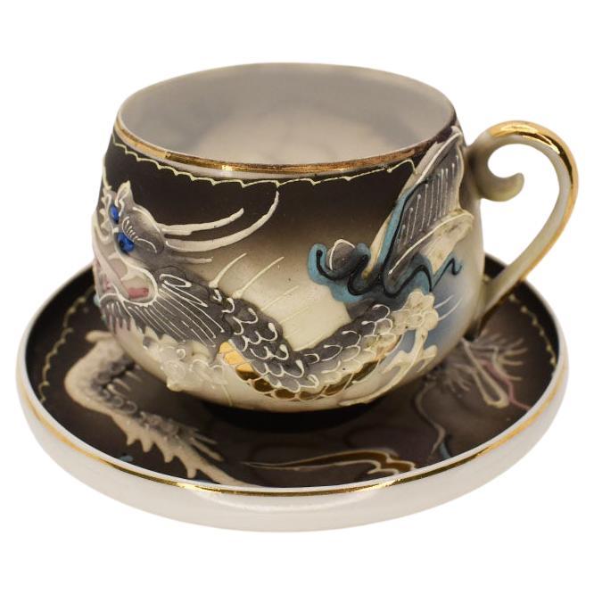 A beautiful artisanal handcrafted porcelain Dragon ware teacup and saucer set. This set features a moriage dragon design. Created from slip and applied around the body of the cup, the eye-catching dragon is hand-painted in a gorgeous blue, back, and