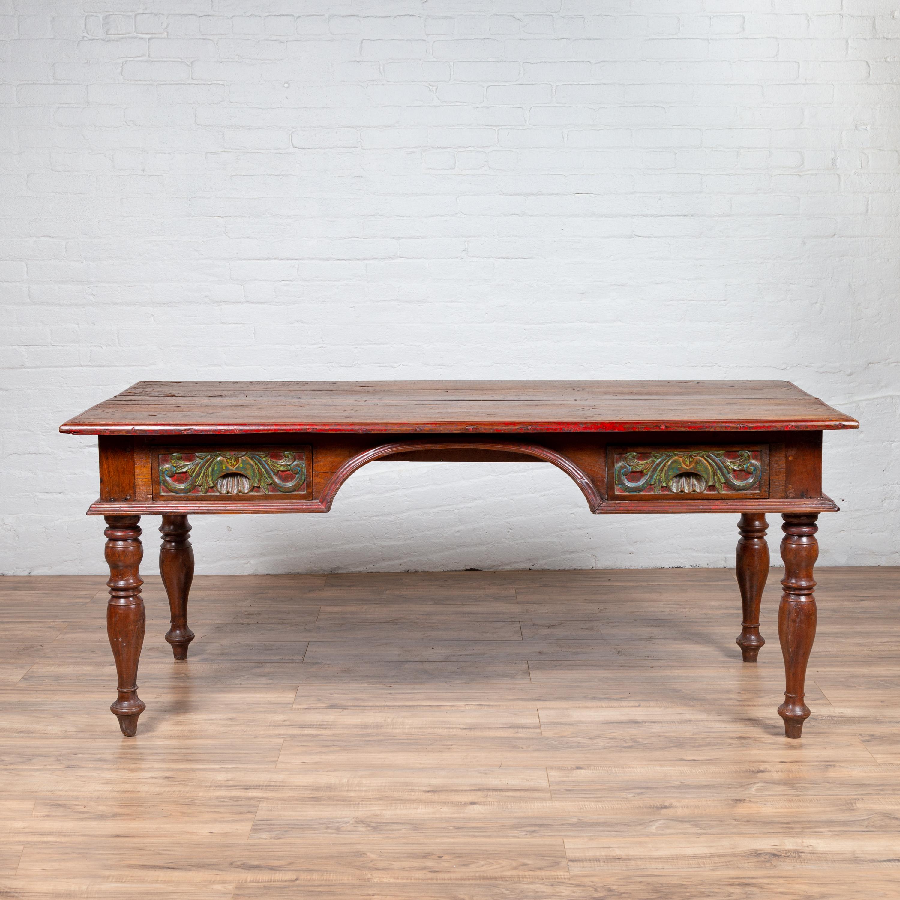 An antique Javanese kneehole desk from the early 20th century, with polychrome finish and carved accents. Born on the Island of Java in the early years of the 20th century, this exquisite writing table features a rectangular planked top with nicely