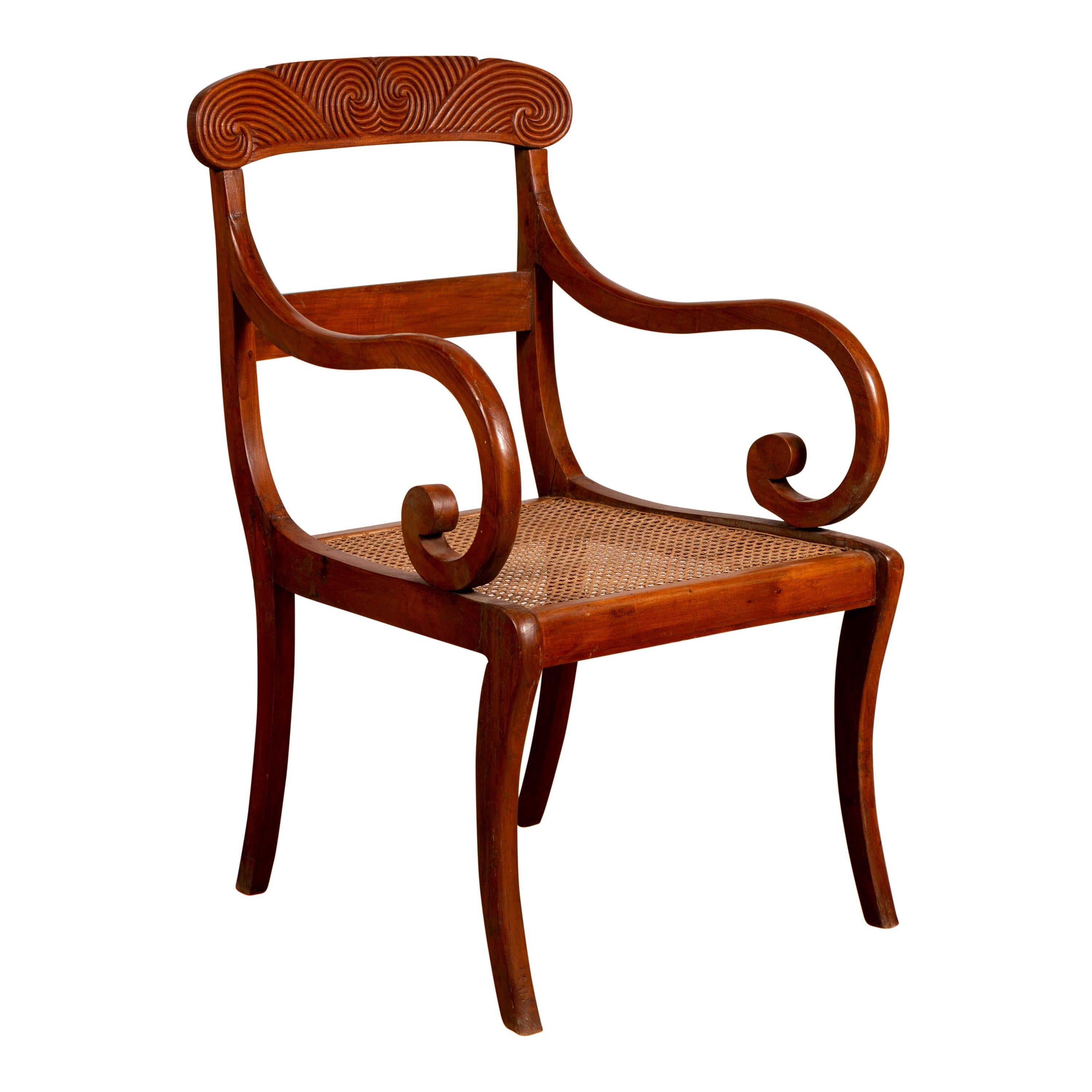 Antique Javanese Wooden Armchair with Carved Back, Curving Arms and Rattan Seat For Sale