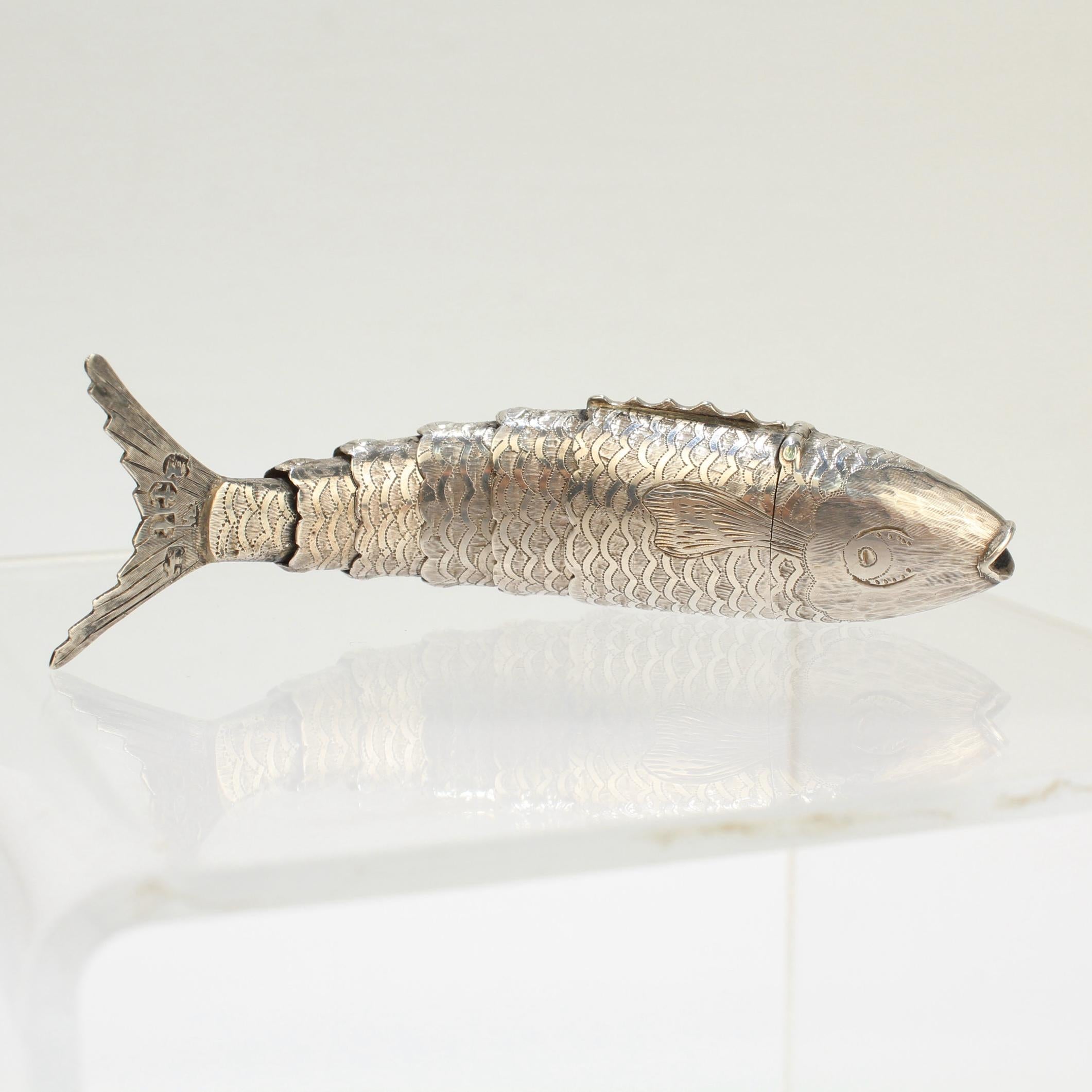  A very fine antique English sterling silver vinaigrette.

In the form of a fish with realistically engraved eyes, fins and scales.

A hinged cover in the form of the fish's head opens to reveal a grille and sponge compartment. The body supports 5