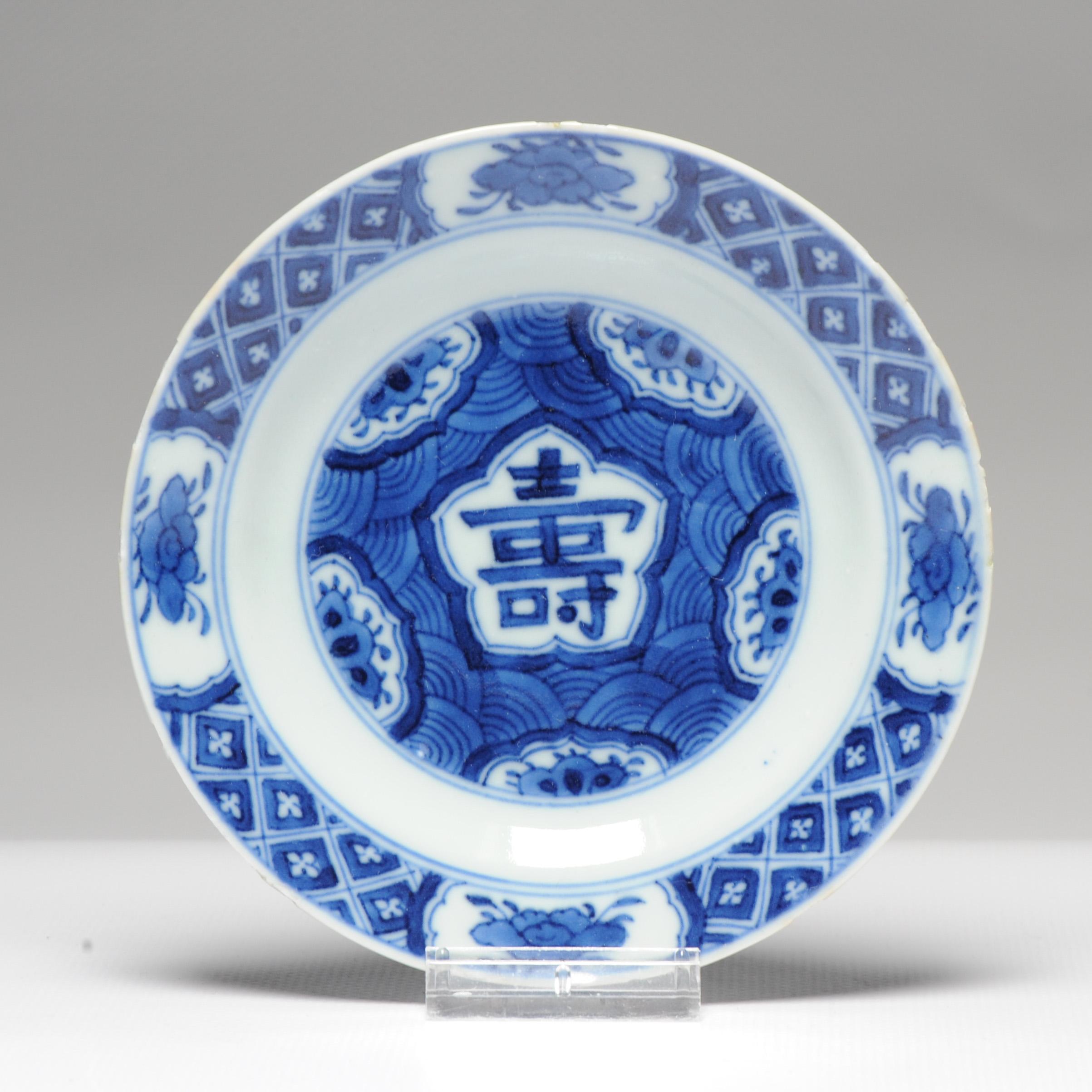 Description

Small plate on footring, wide, slightly upturned rim. Decorated in underglaze blue. In the centre a fish-scale pattern with five reserved, lobed half-
panels with a flower, in the centre a lobed panel with the character shou (long