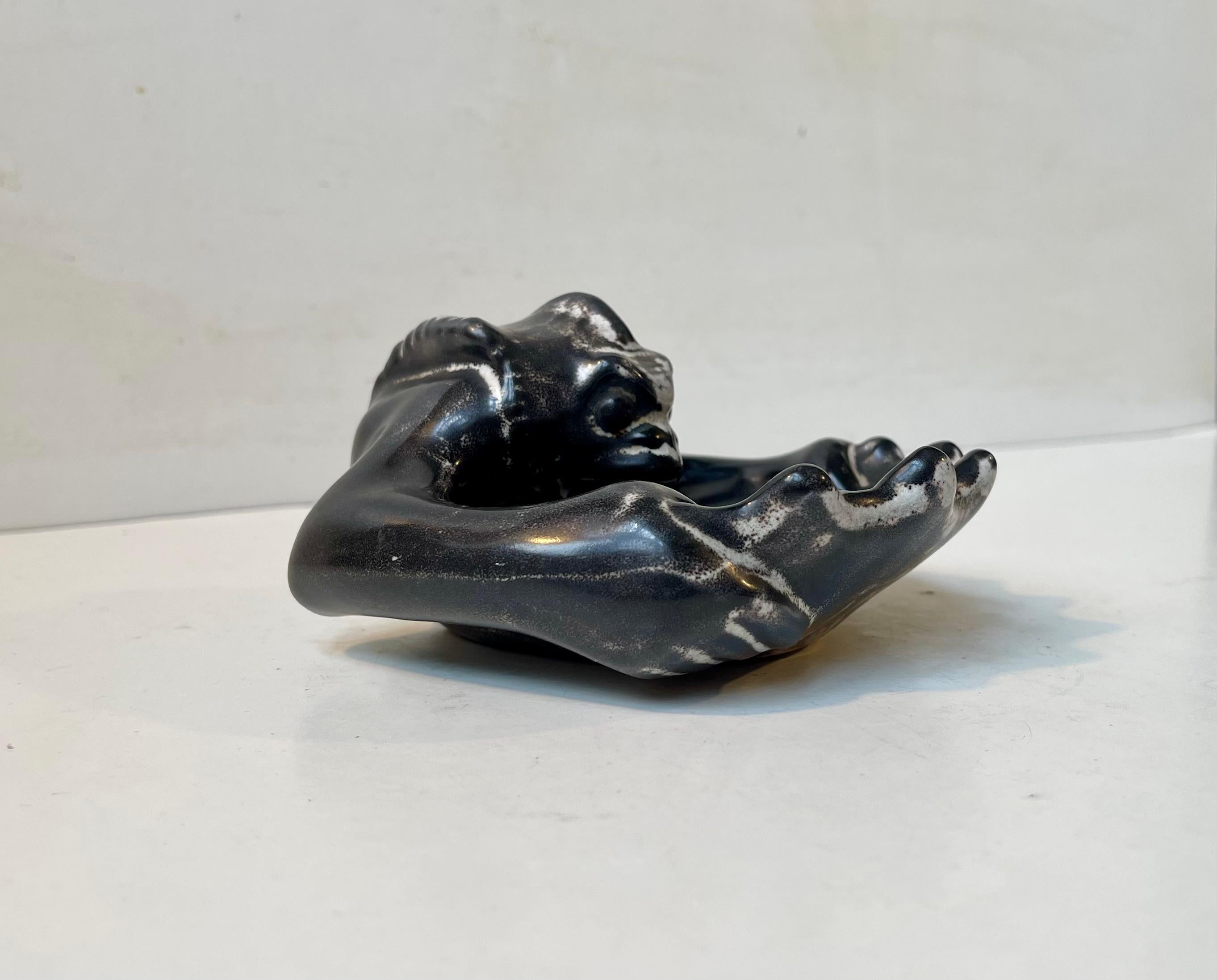 Petit plat en céramique sculptée représentant un diable ou un démon émergeant d'une coquille de palourde. Conçue et réalisée par l'artiste et sculpteur danois Karl Hansen Reistrup, qui fut le chef artistique du studio Herman A. Kähler au Danemark de