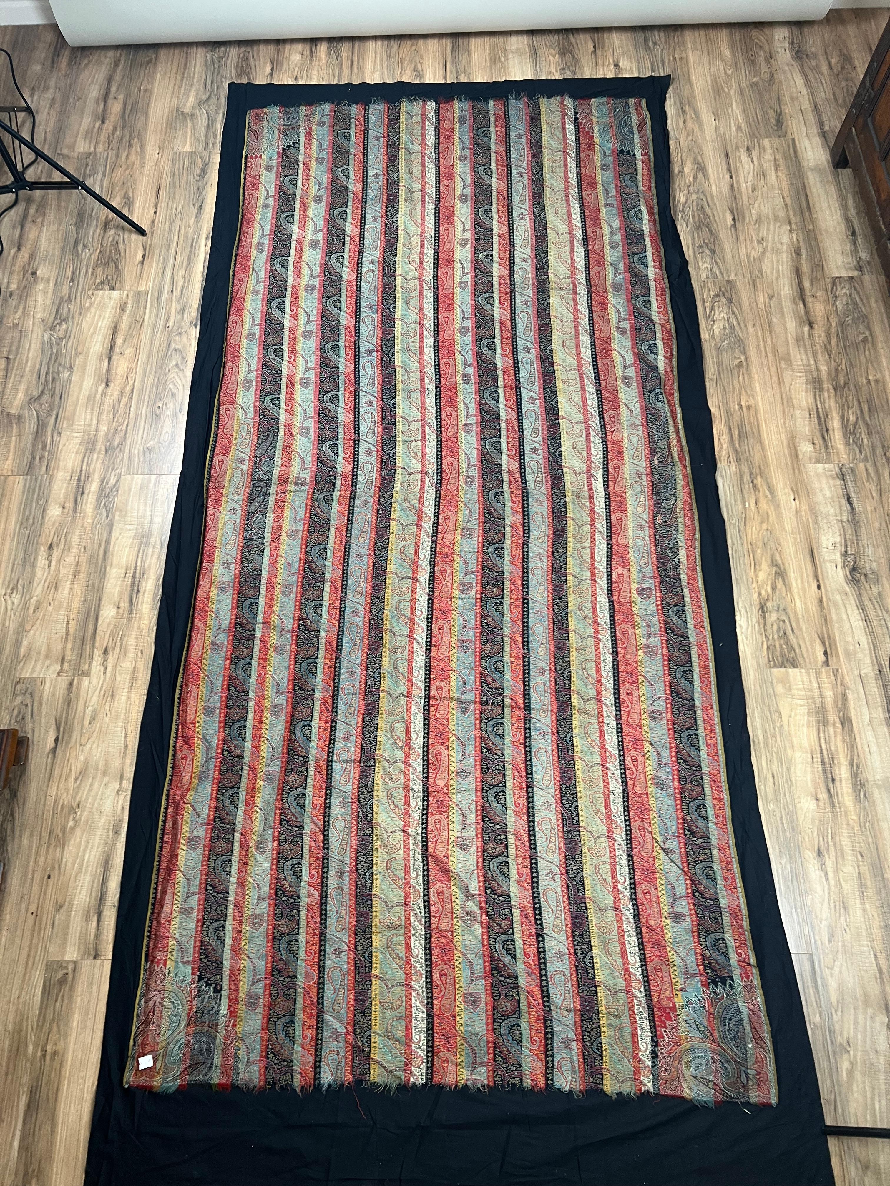 Ce châle ancien en laine du Cachemire présente une étonnante disposition de rayures verticales remplies de motifs boteh (paisley) colorés, tissés dans des rouges, des verts, des bleus et des ivoires doux. Le champ rayé est à la fois vif et raffiné,