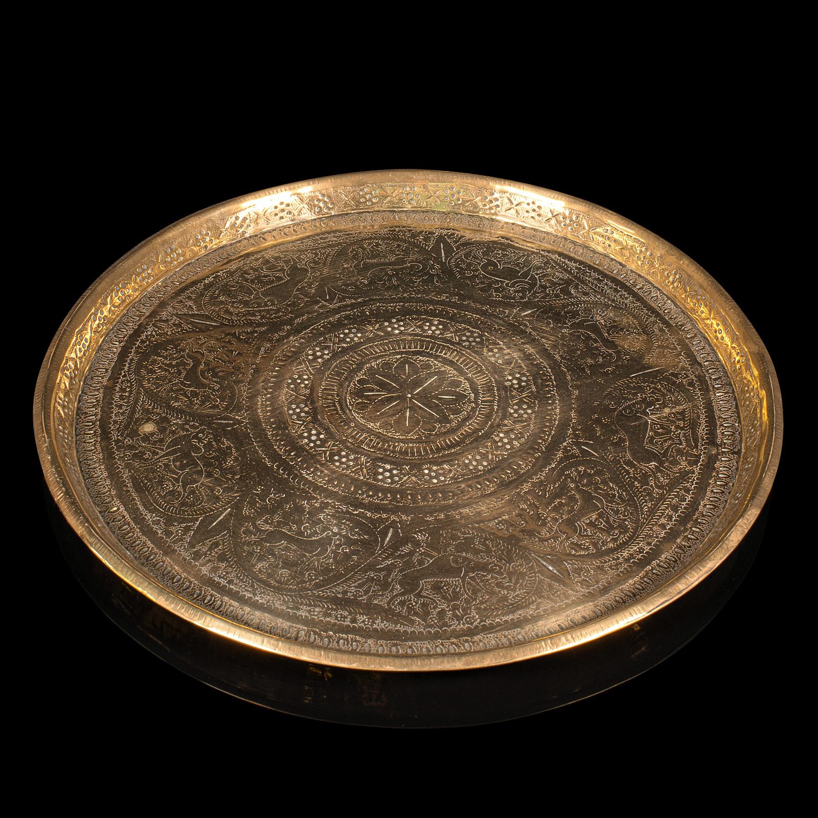 
Se trata de una antigua bandeja decorativa Kasmiri. Bandeja india de latón grabado, de finales de la época victoriana, hacia 1900.

Un fascinante grabado adorna esta distintiva bandeja de servir
Presenta una deseable pátina envejecida y en buen