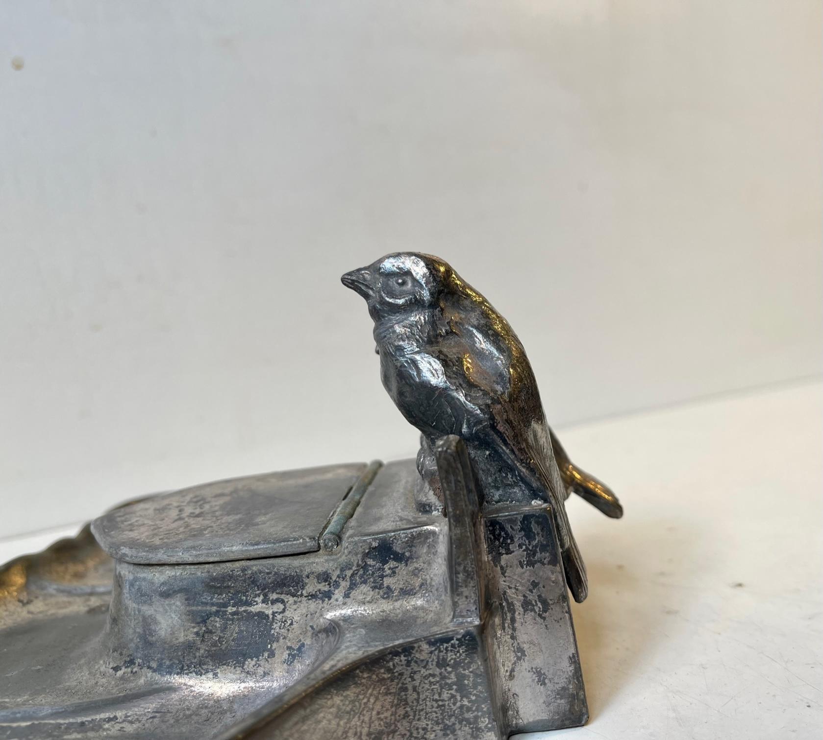 Decorative inkwell with two small lovebirds and original ink-glass. Manufactured by Kayserzinn in Germany circa 1910. It features a rustic authentic patina and the original silver-plating has largely worn of giving it character and charm.