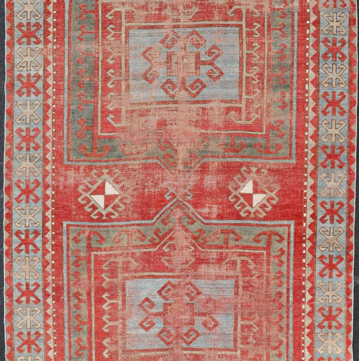 This antique Kazak hand-knotted rug features a geometric double box design and is enclosed within a complementary, multi-tiered border. The rug is rendered in blue, cream, red and brown tones; making this rug a perfect fit for a variety of classic,