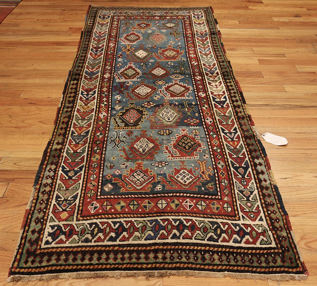 Known for their rich colors, and bold, large-scale design this antique Kazak Caucasian rug lives up to its repertoire. Its geometric boteh designs done in variations of blues and green are contrasted with lively ivory and orange coloring. A rug from