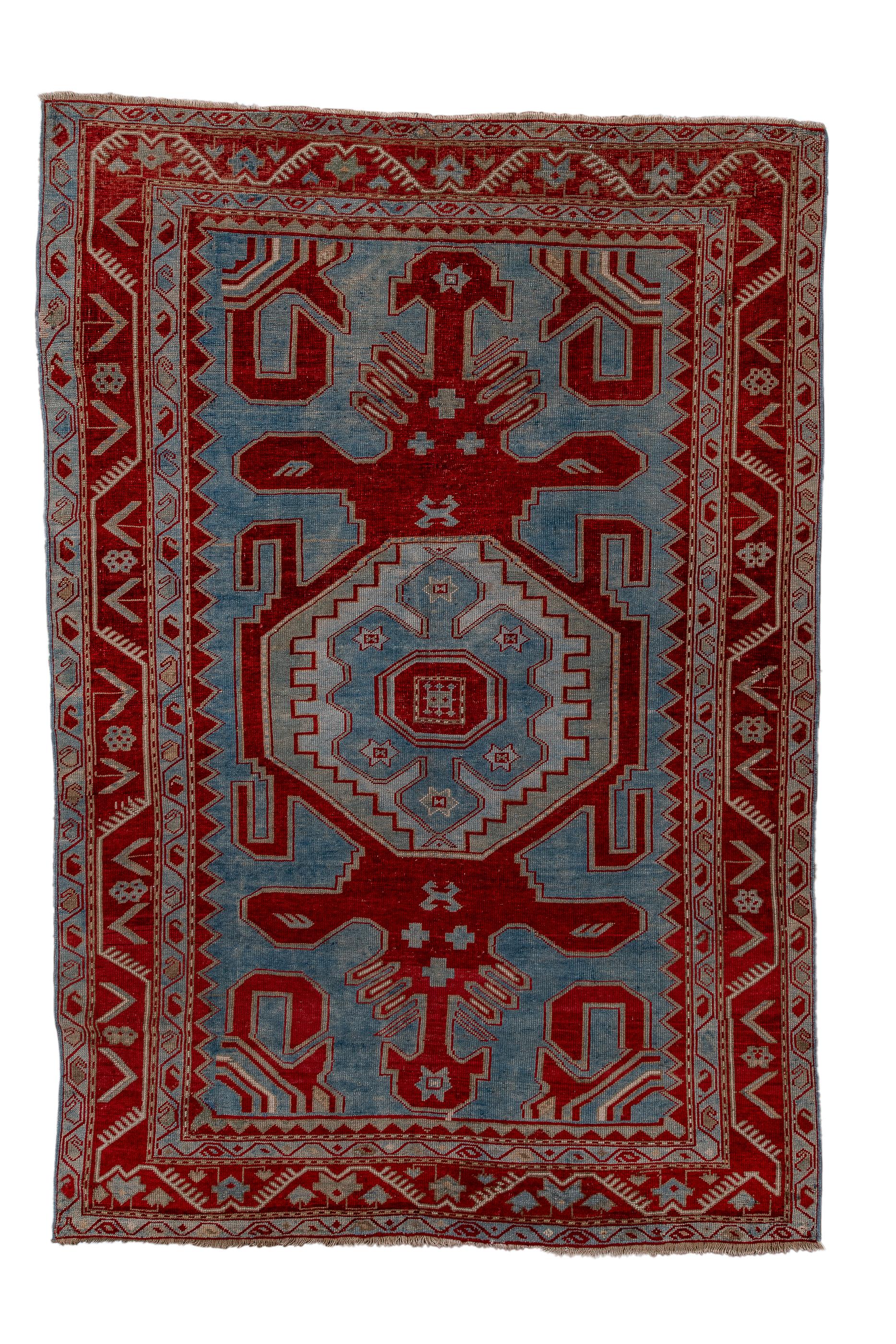 This bold study in dark red and light blue shows an octagonal central medallion enclosing a stepped ecru panel and centred by a light blue, lobed sub-medallion. Powerful red geometric volutes curve in from the corners. Main red border with rosettes
