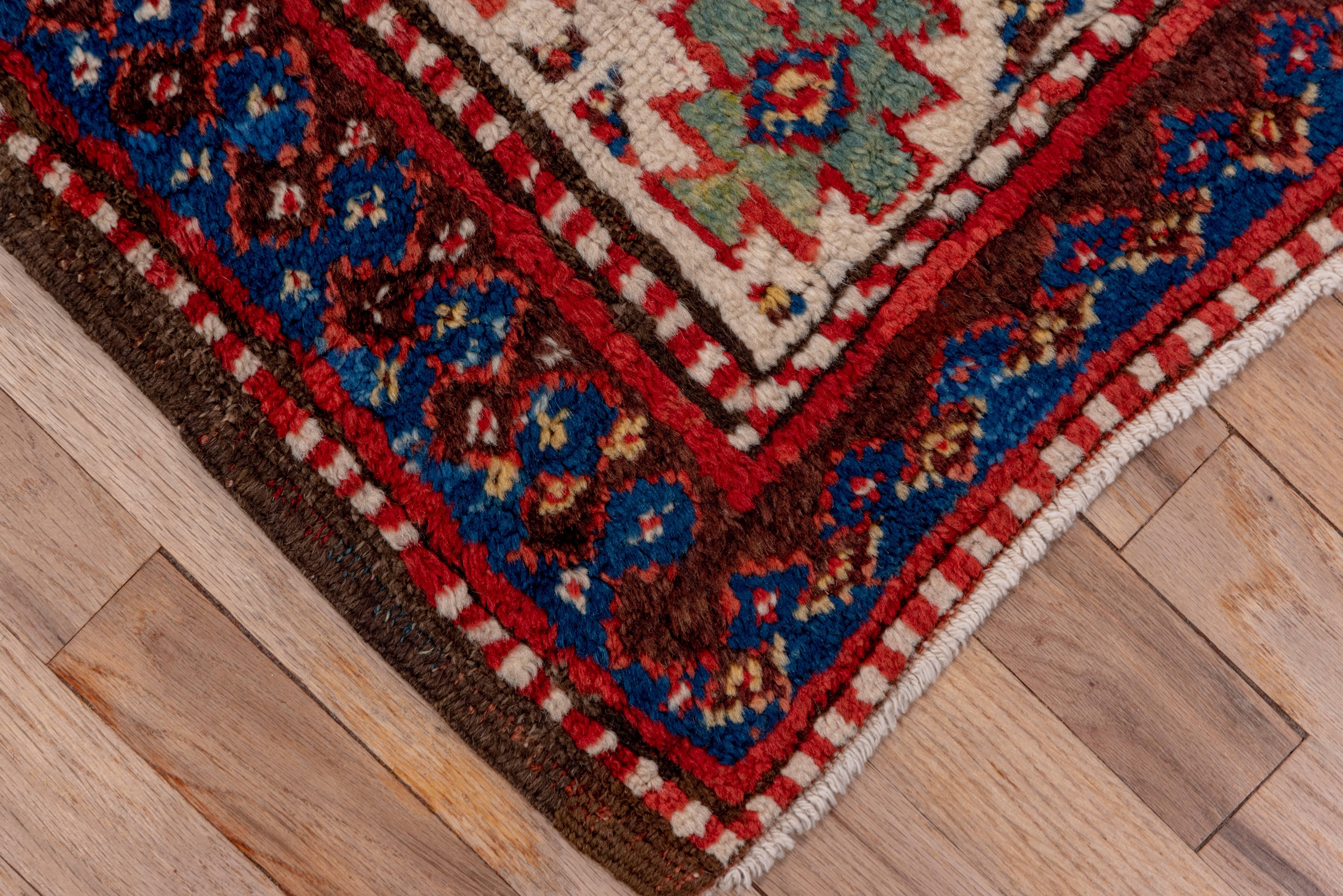 This good condition south Caucasian rug displays a madder red field with a pole medallion of five navy, ivory and green lozenges. An ivory border with floating ashiks is flanked by keyhole pattern bitonal reciprocal guards. The colors are all of