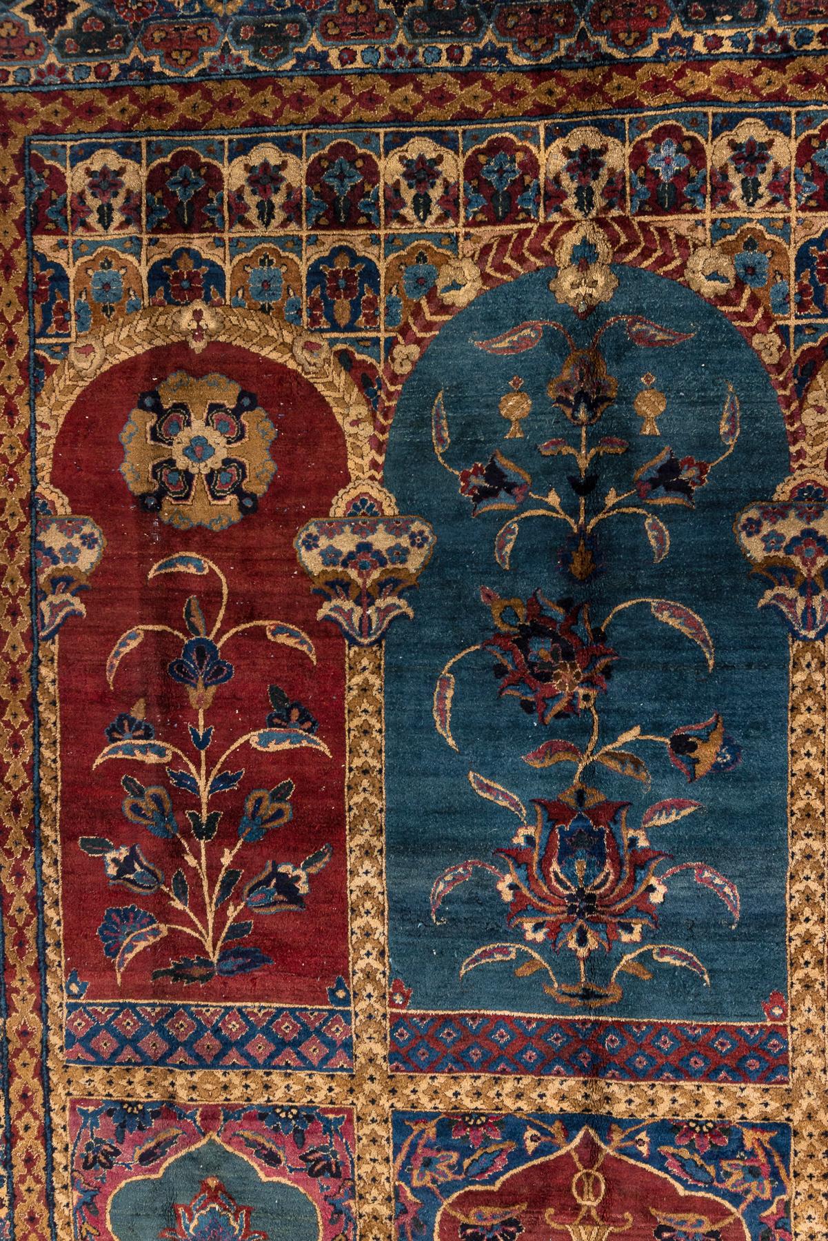 Ce tapis ancien de Kerman présente une disposition architecturale frappante des panneaux, composée de niches arquées remplies de motifs floraux et d'ornements symboliques. Les riches tons de rouge profond, de bleu lagon et d'or antique créent un