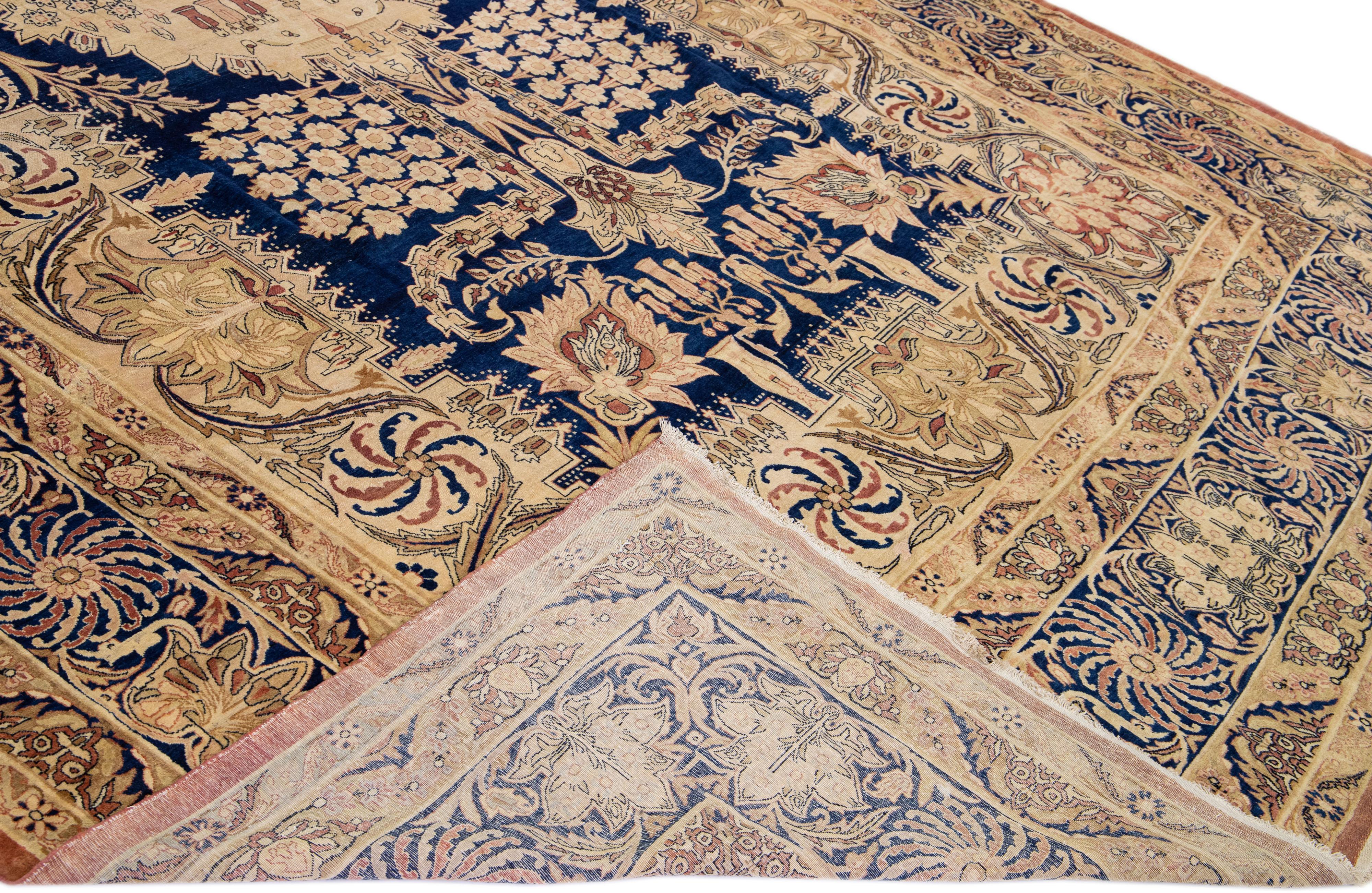 Magnifique tapis antique Kerman en laine nouée à la main avec un champ beige. Ce tapis persan présente des accents bleus et bruns dans un magnifique motif floral en médaillon.

Ce tapis mesure : 11'5
