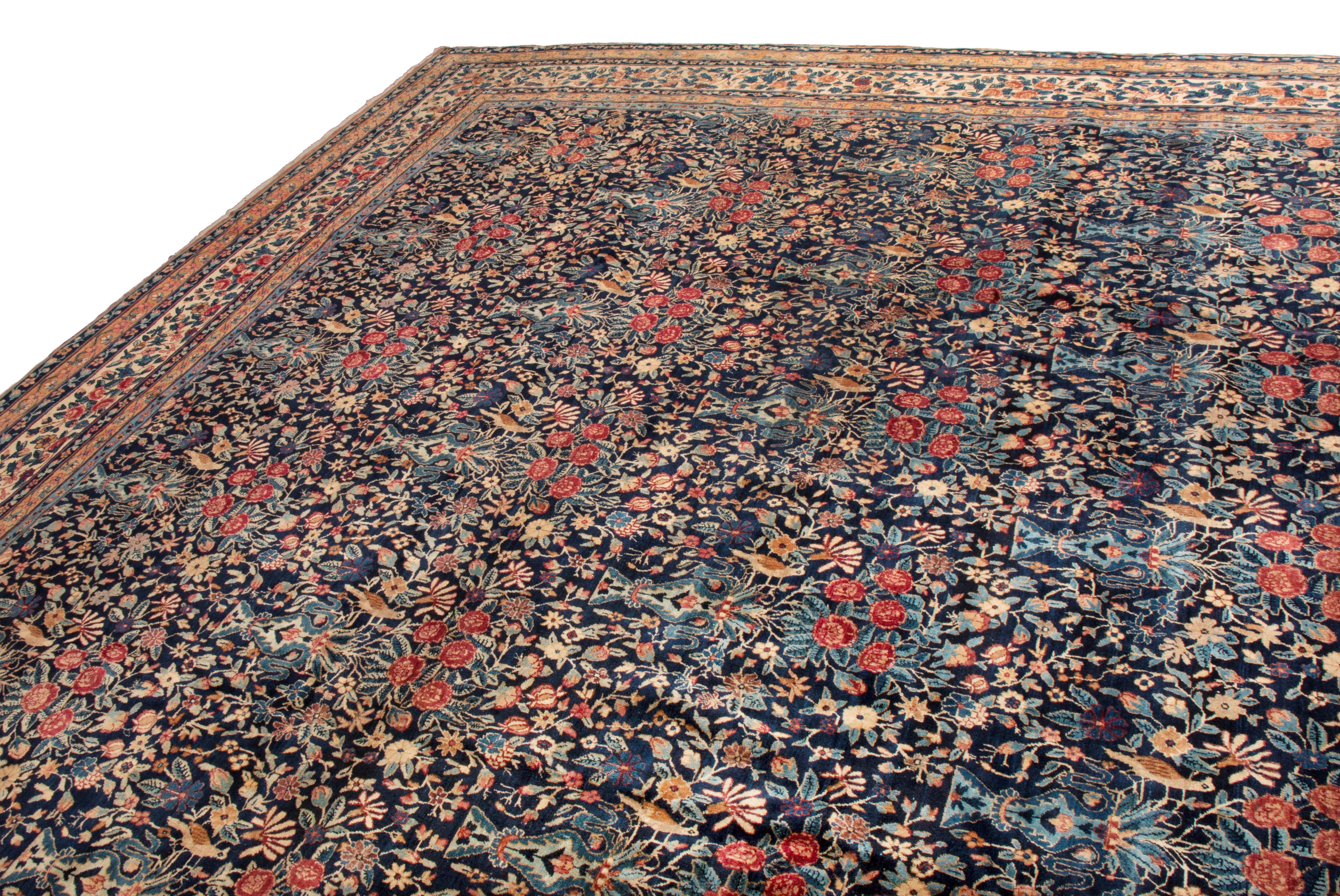 This antique Kerman Lavar Persian has an all-over floral pattern with a traditional style. From 1910-1920, the many variant flowers in the field depicted hanging from green and blue vases, are a staple of designs from Lavar (also known as Ravar) in