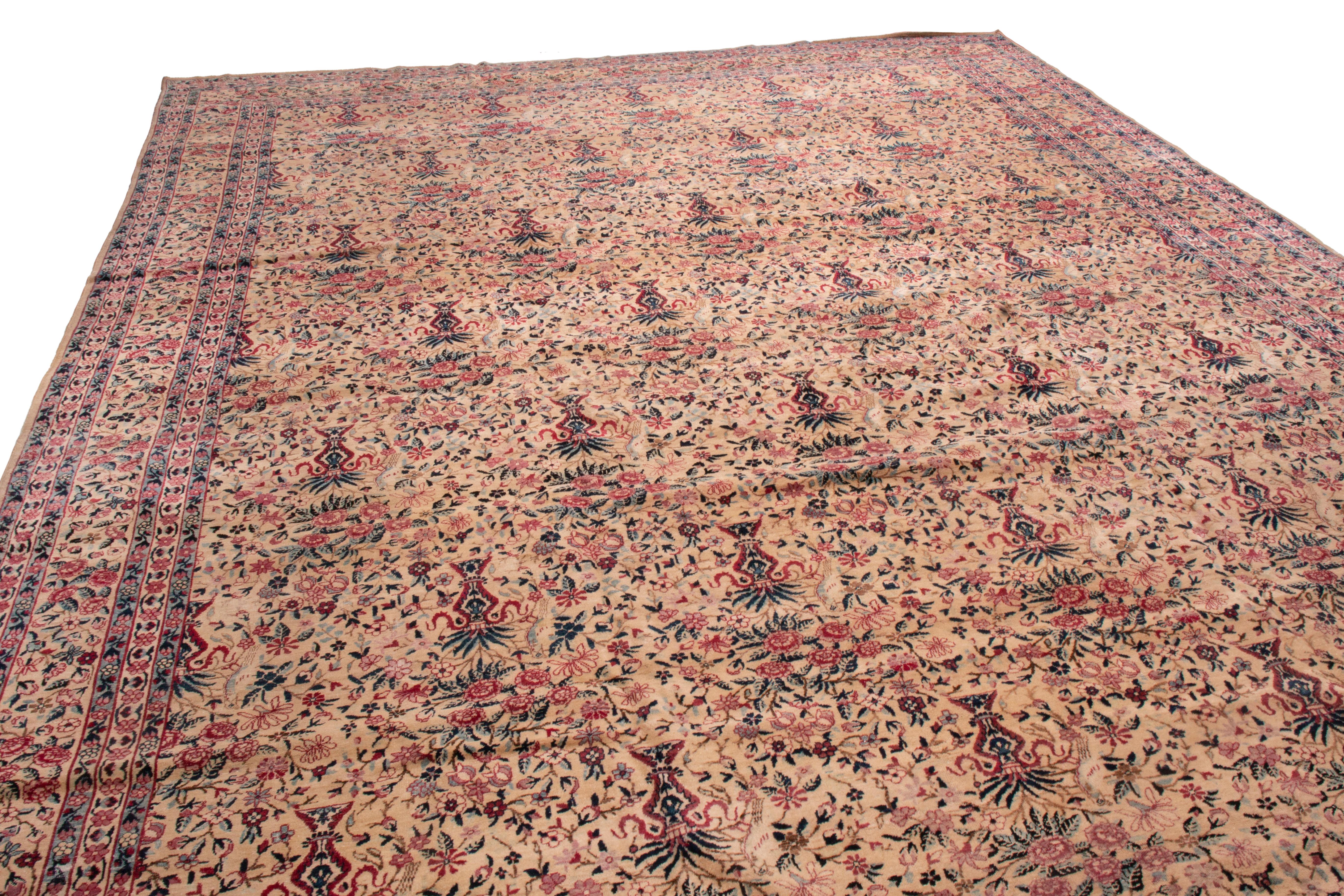 This antique Kerman Lavar rug is influenced by the Victorian era, the all-over field design depicts traditional floral vases and birds in purple, red, and green, though the vine scroll throughout the border isolates darker purple hues. This is a