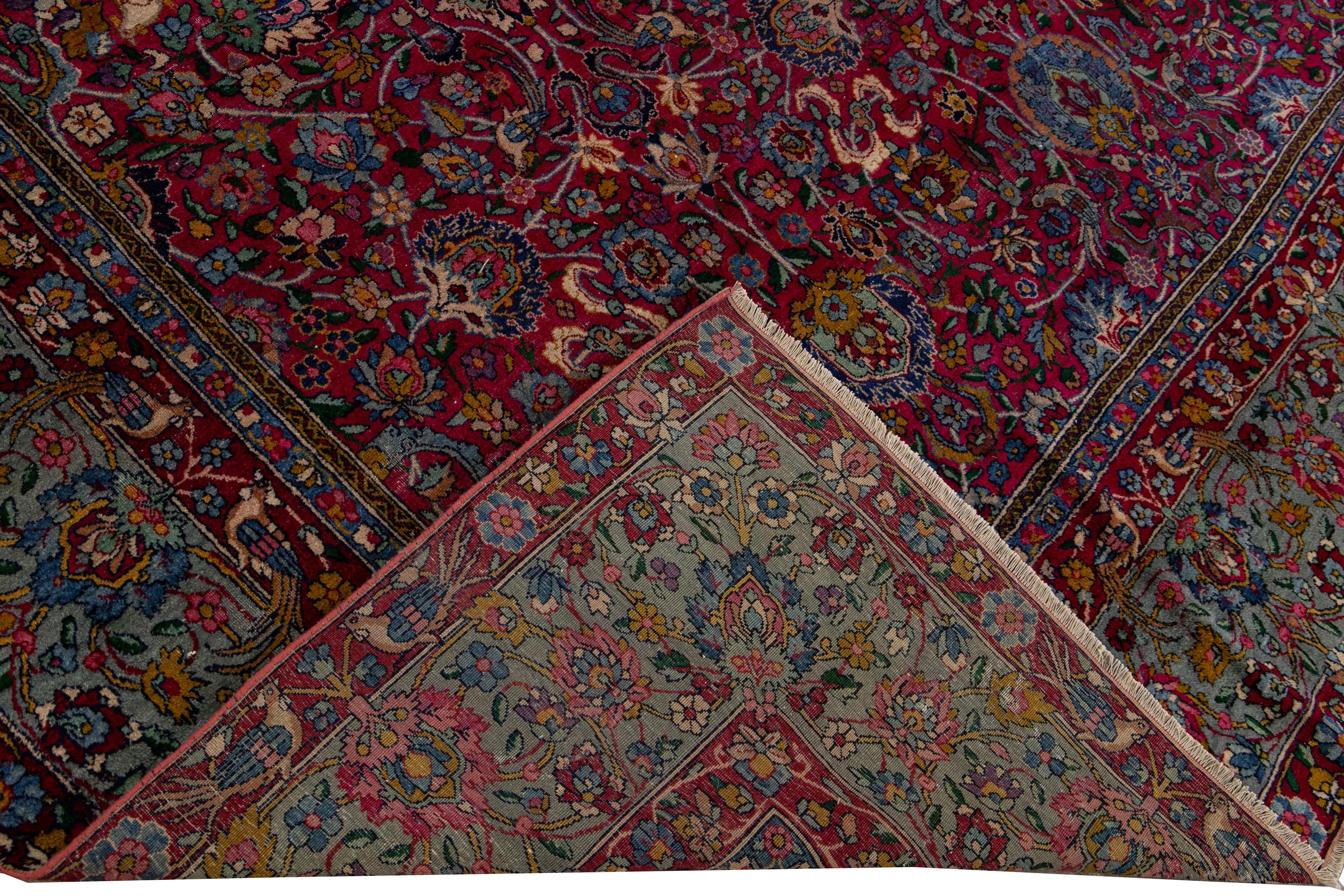 Beautiful antique Kerman hand-knotted wool rug with a red field. This Kerman rug has a blue frame and multi-color accents in a gorgeous all-over botanical floral design. 

This rug measures: 9'7
