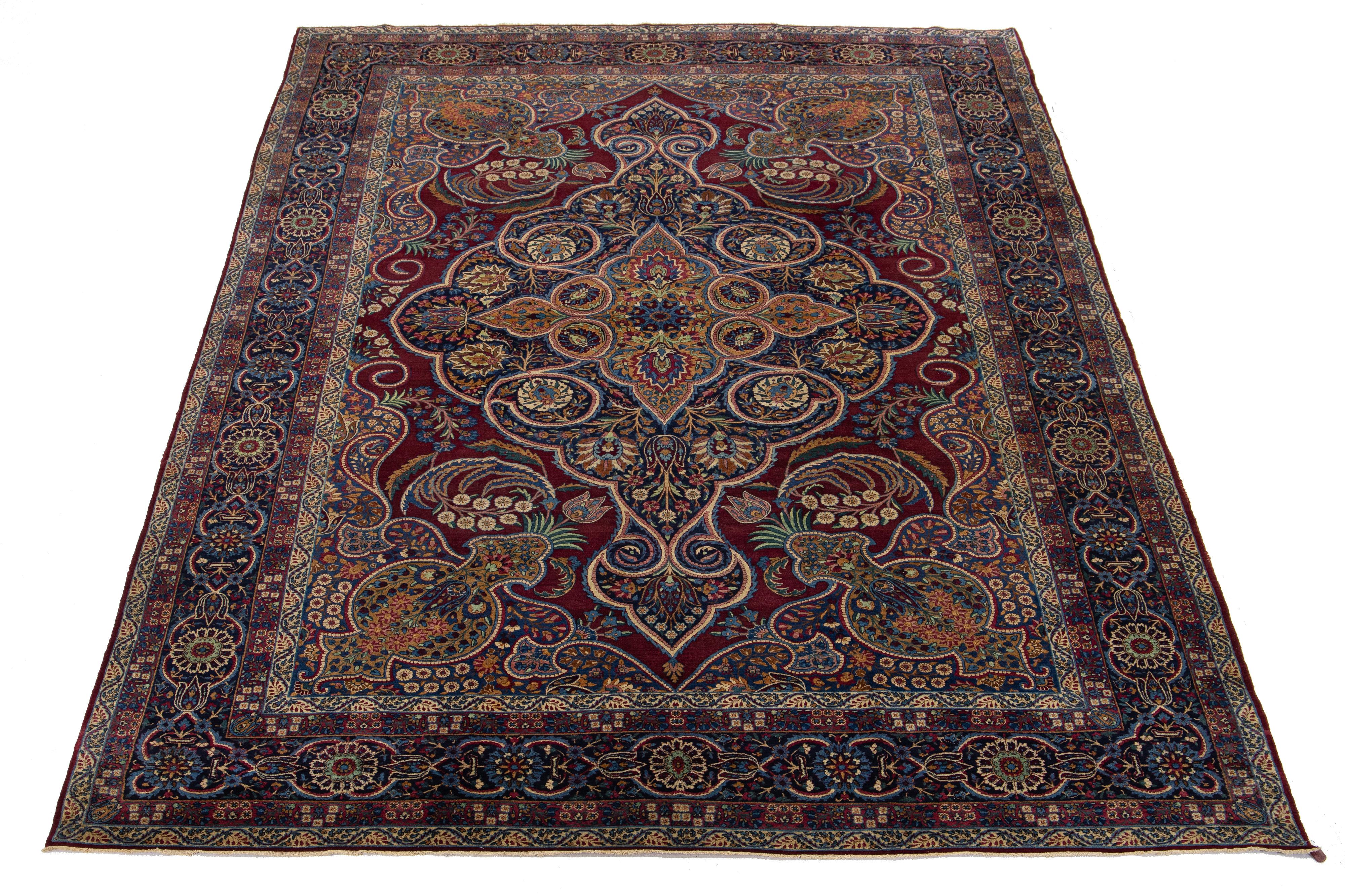 Ce tapis en laine noué à la main est une exquise antiquité des années 1900. Son ravissant design floral aux multiples couleurs orne gracieusement un riche fond rouge, ce qui en fait un ajout intemporel à n'importe quelle pièce.

Ce tapis mesure 9'8