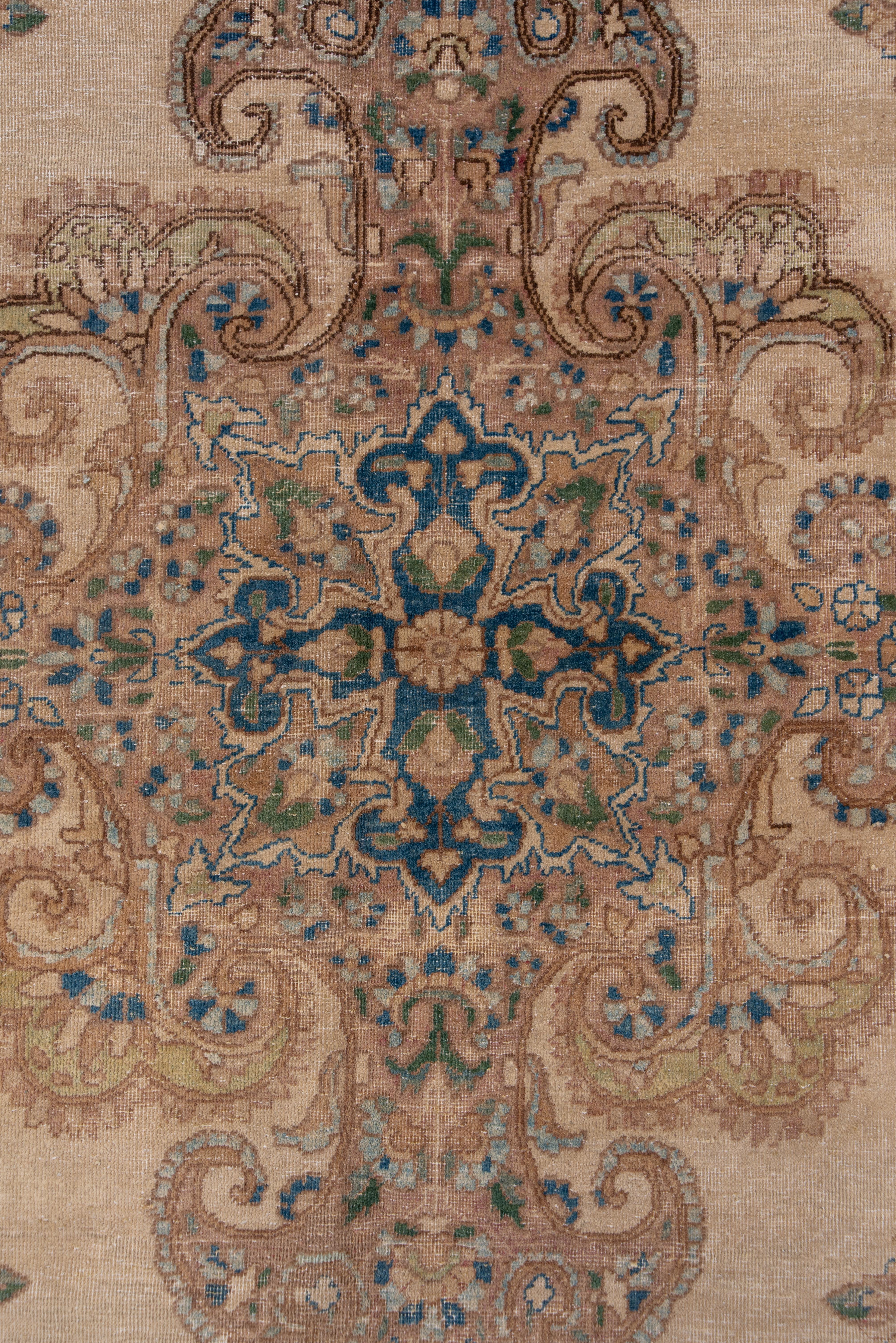 This predominantly light colored SE Persian city rug has an old ivory field with a sharply involuted cruciform four pendanted medallion with a light blue centre. The corners point toward the centre with floriated palmettes. The beige ivory border