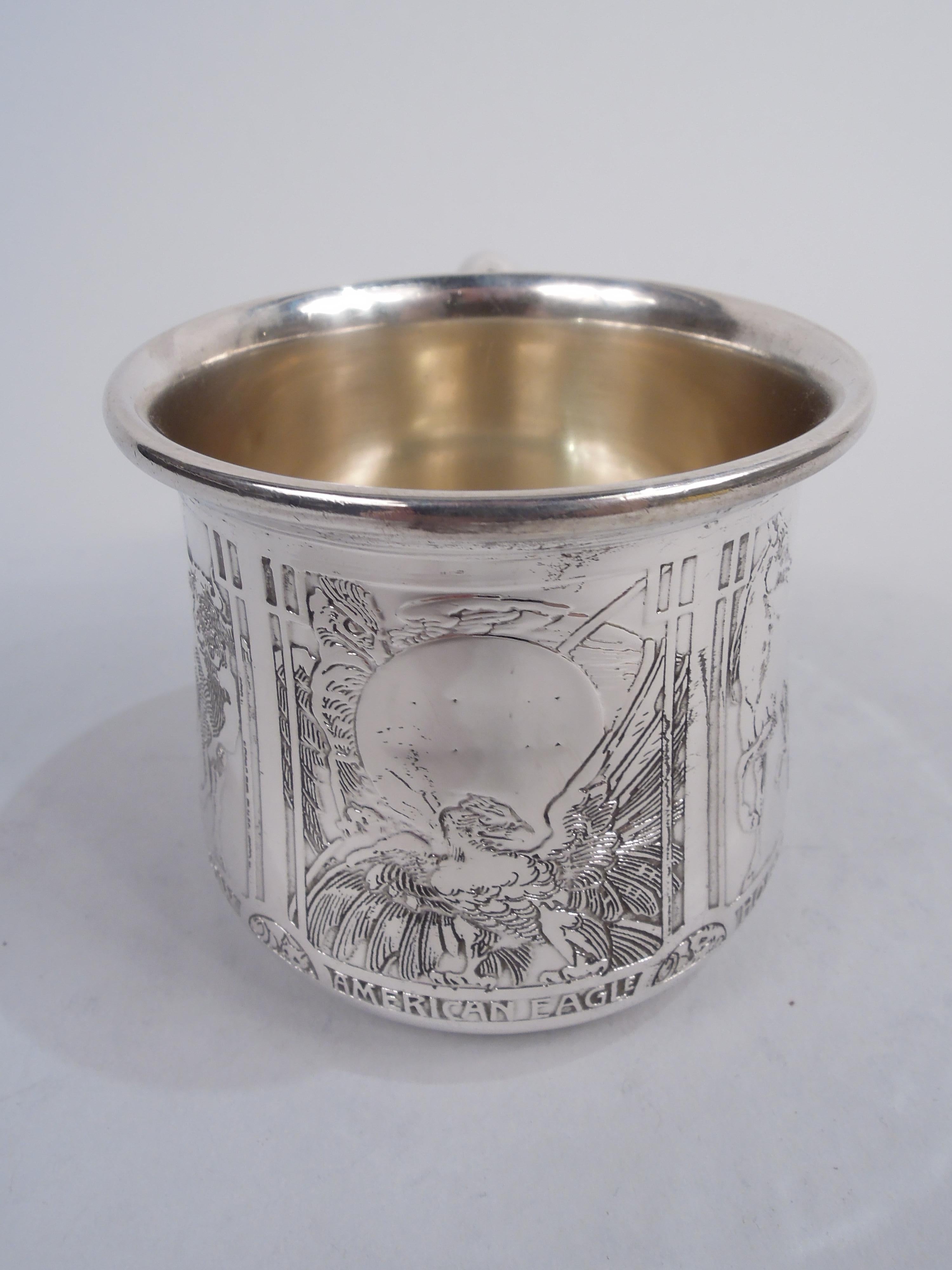 Edwardian sterling silver baby cup. Made by William B. Kerr in Newark, ca 1915. Upward tapering sides and scroll handle. Acid etched frames with animals, including an elephant, camel, and gazelle. Frame with American eagle has vacant space for