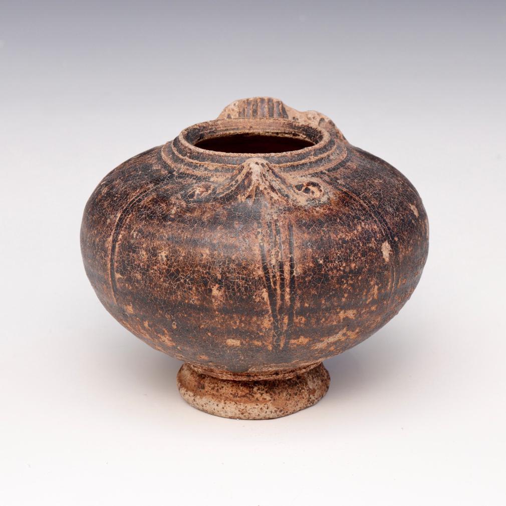 Khmer Ceramic Lime Pot. A squat globular stoneware jarlet with a high shoulder in the form of a bird covered in a  brown glaze stopping short of the elevated foot displaying the beige biscuit, a owl’s beak and eyes in relief on the shoulder and 