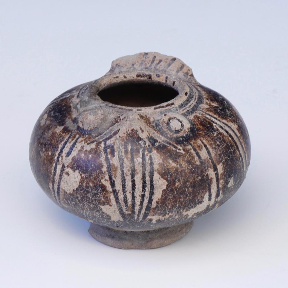 Khmer Lime Pot. A small squat globular stoneware jarlet in the form of a bird covered in a brown glaze stopping short of the elevated  foot displaying the sandy beige biscuit, an owl’s beak and protruding eyes in relief on the shoulder and a pinched