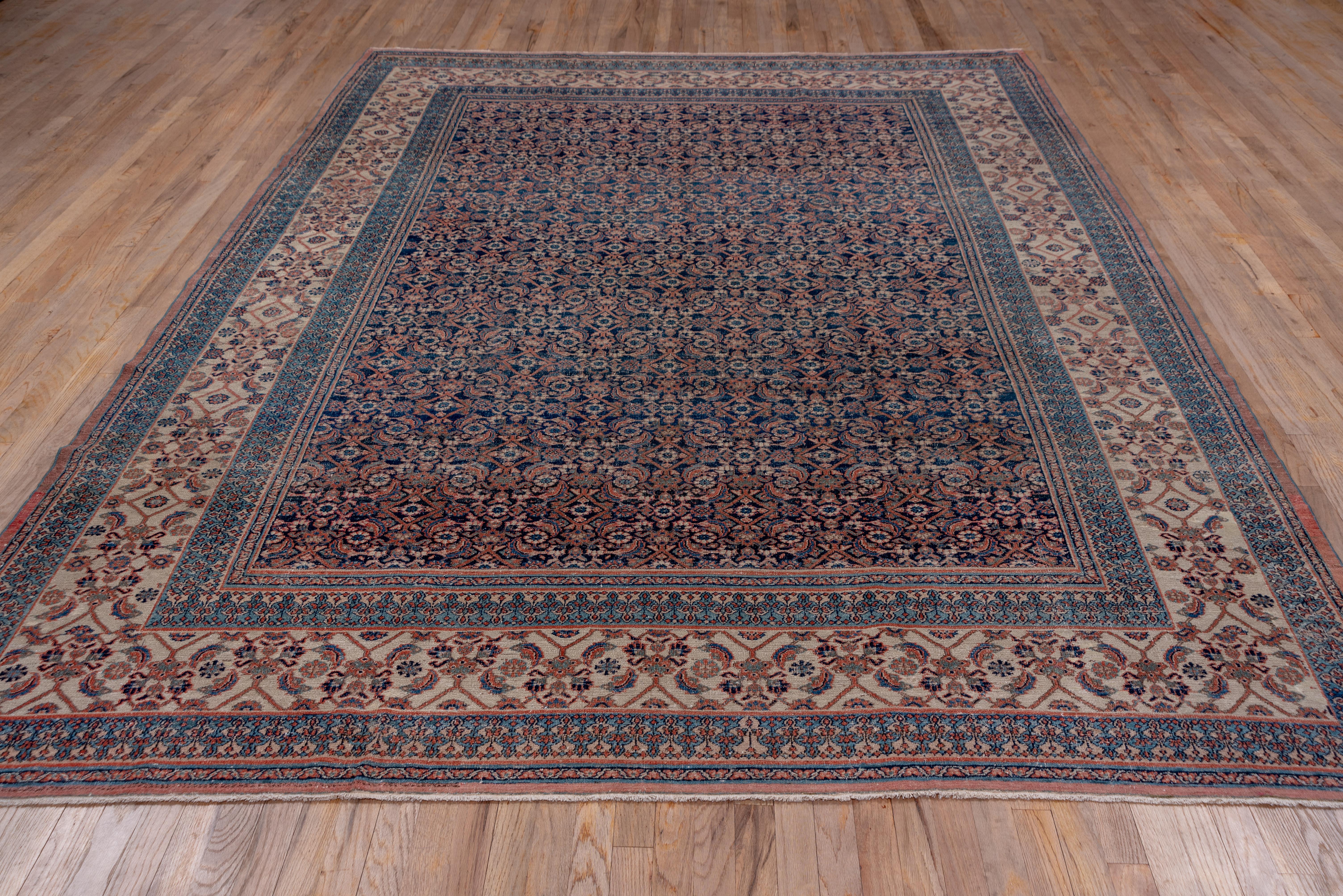 This well-worn NE Persian city carpet shows a dark blue ground supporting a close Herati pattern accented in ivory and soft red. The unusual ivory main border has an open-out Herati design emphasizing rosettes in open diamonds.