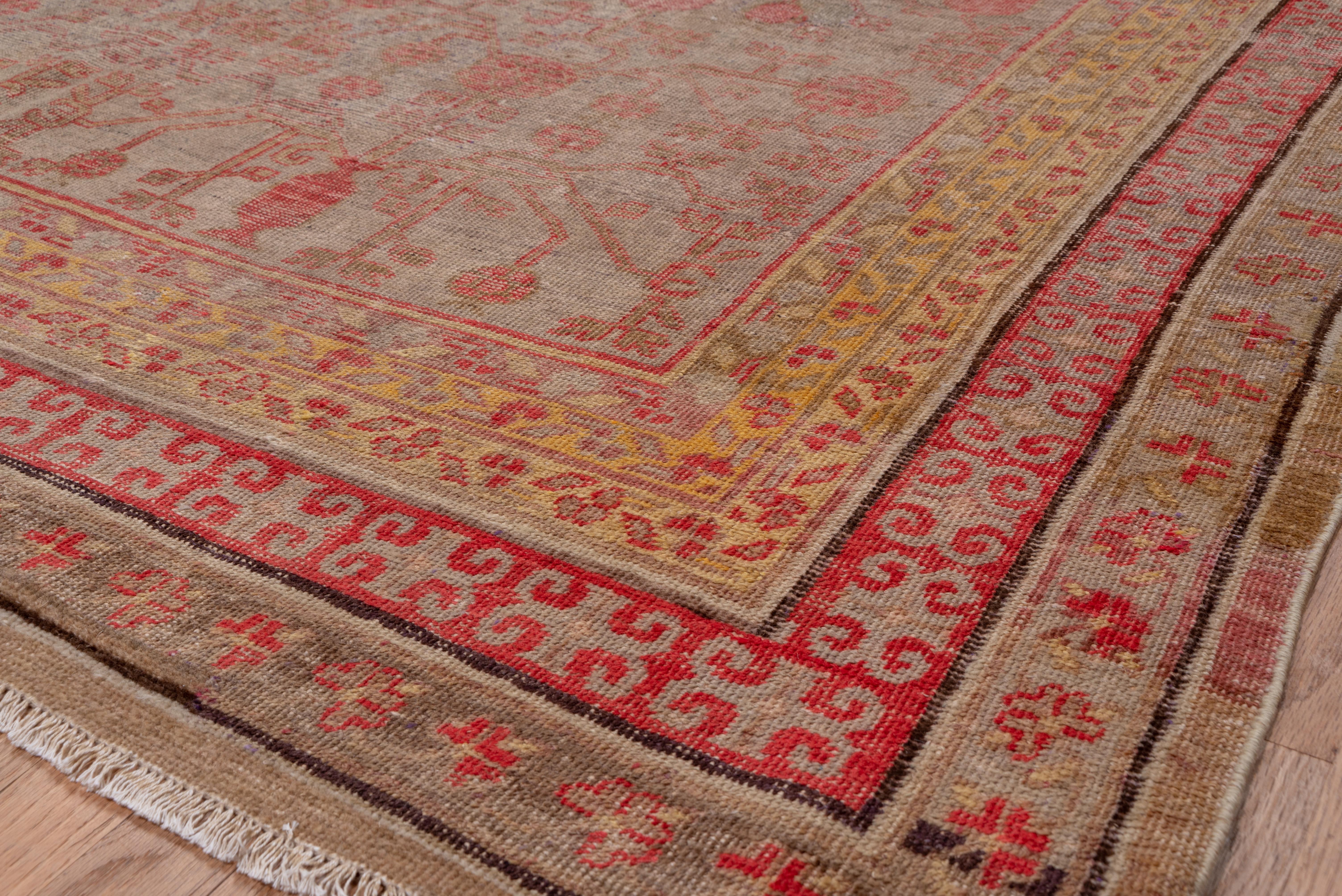 Das blassviolette Feld dieses Khotan-Teppichs zeigt vier winzige Vasen, aus denen zwei fruchttragende, eckige Granatapfelbäume in einem traditionellen Muster innerhalb einer blassgelben Blattbordüre wachsen.