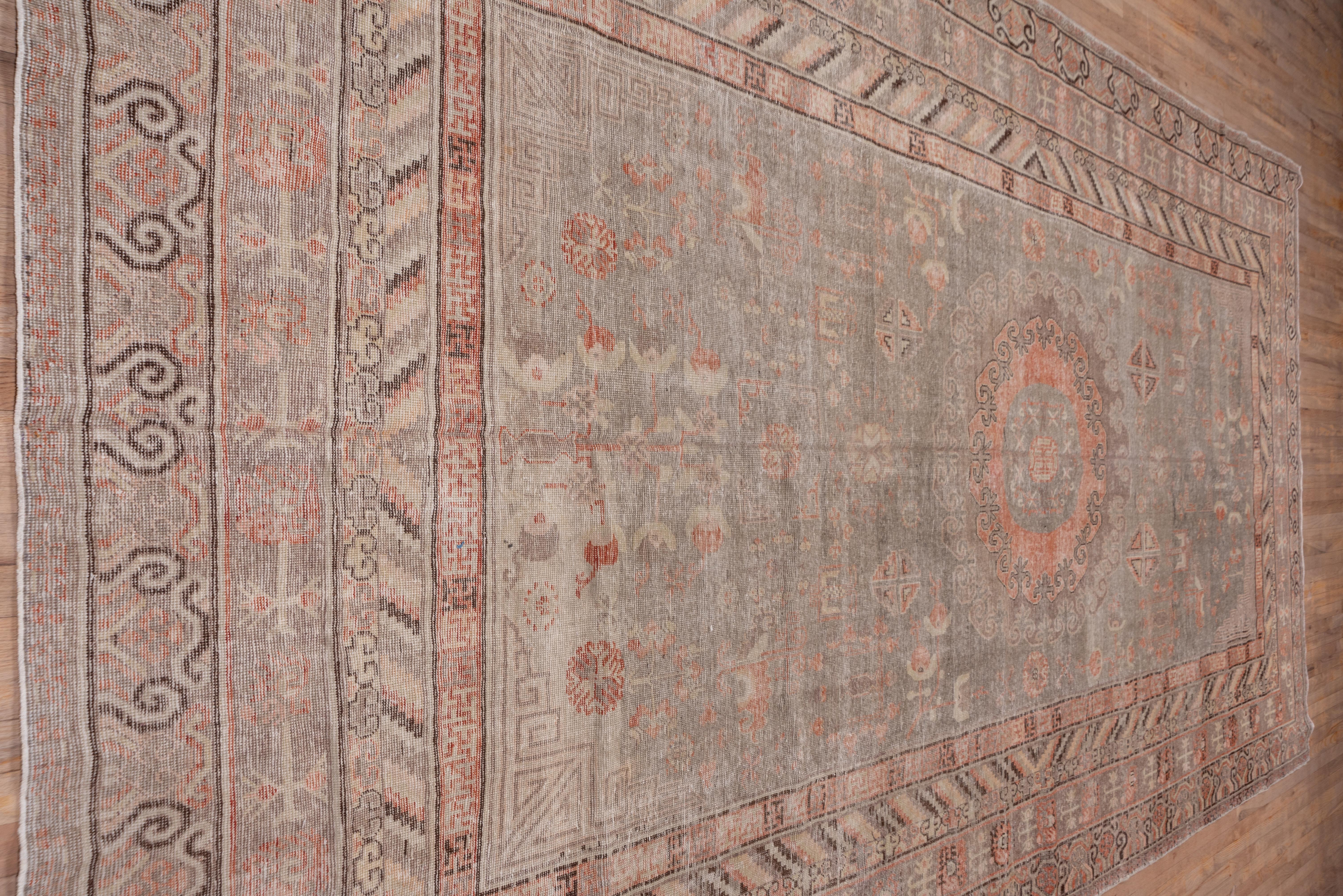 This mellow ton Xinjiang oasis town carpet features a double concentric round medallion with a reciprocal edge on the buff ground. Chinese style fret corners, small divided octagons and bent leaves adorn the field of this worn flat piece with a