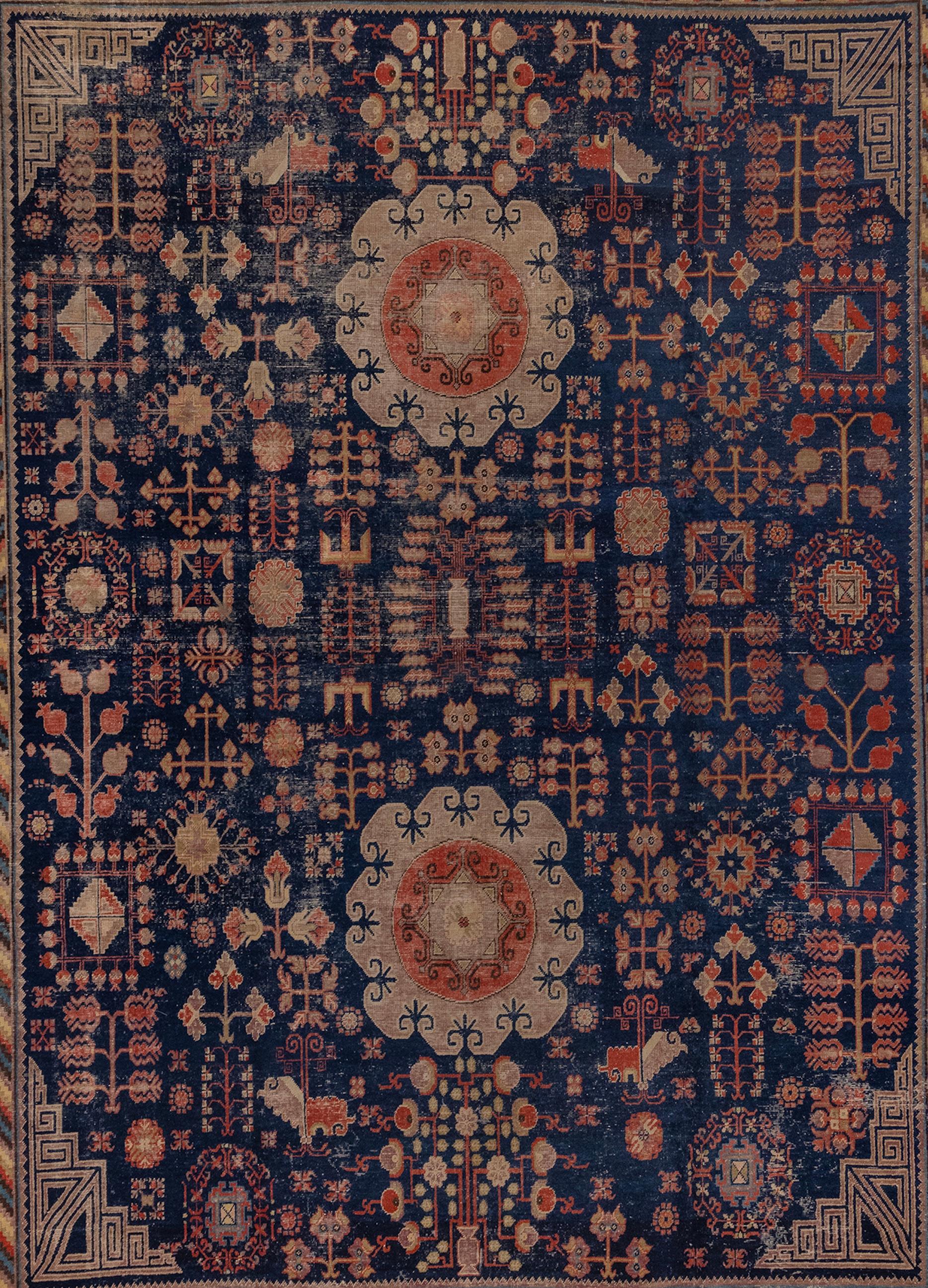 Magnifique tapis Khotan avec des médaillons uniques et un motif d'arbre de vie. La bordure est joliment détaillée avec des rayures colorées et des symboles de grenade. Il s'agit d'un grand tapis, rare pour ce style de Khotan.