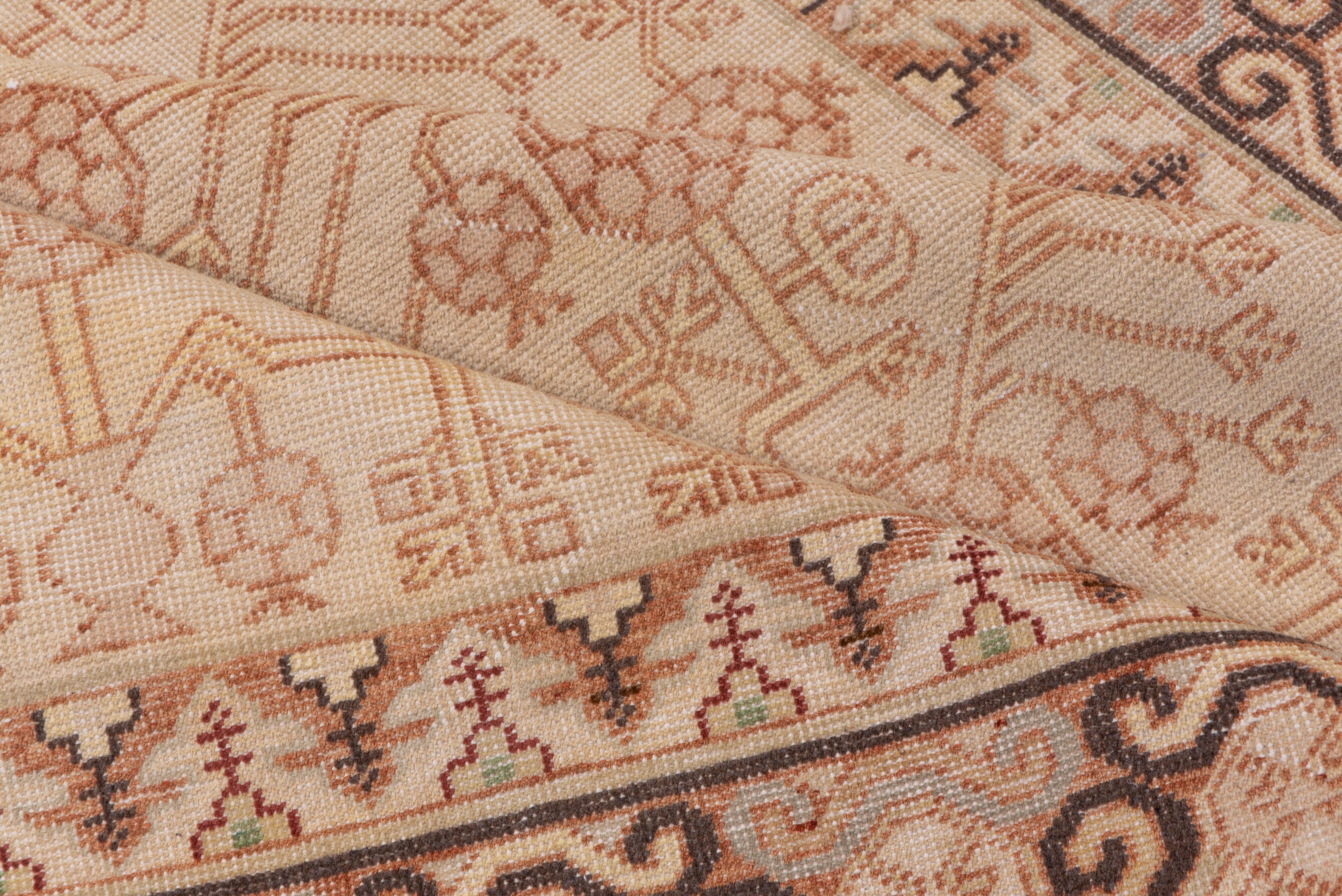 A two column stylized pomegranate tree design with tiny end vases fills the oatmeal field of this Xinjiang town rug with a dark brown - accented partial Yun-tsao Tou border. Pink tones, neutral field.