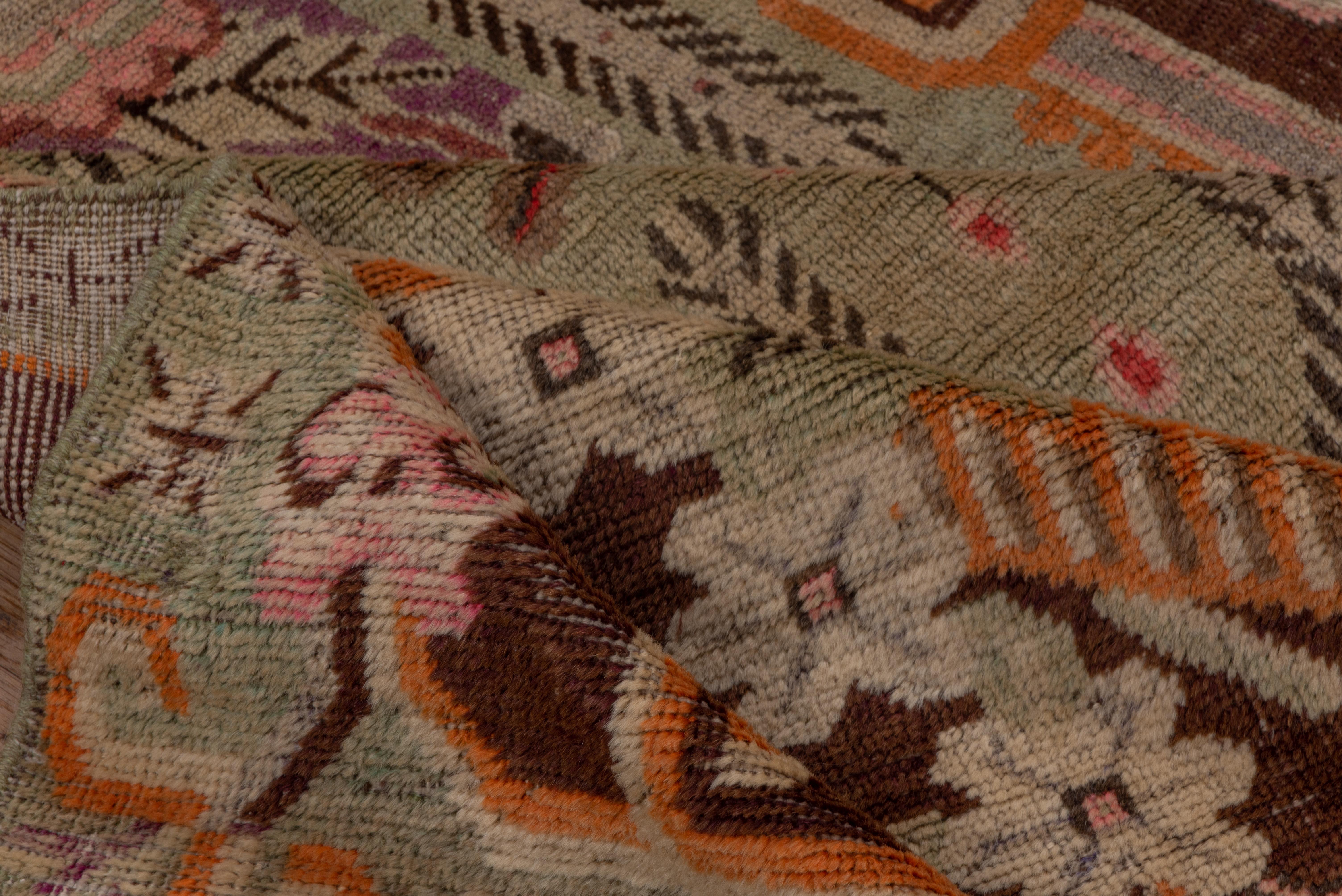 In a bold style reminiscent of NW Persian Heriz rugs, this Xinjiang town scatter shows a tall cartouche medallion enclosing pomegranates, within mauve and red corners with boldly barbed ecru leaves. Straw accents. Narrow geometric borders.