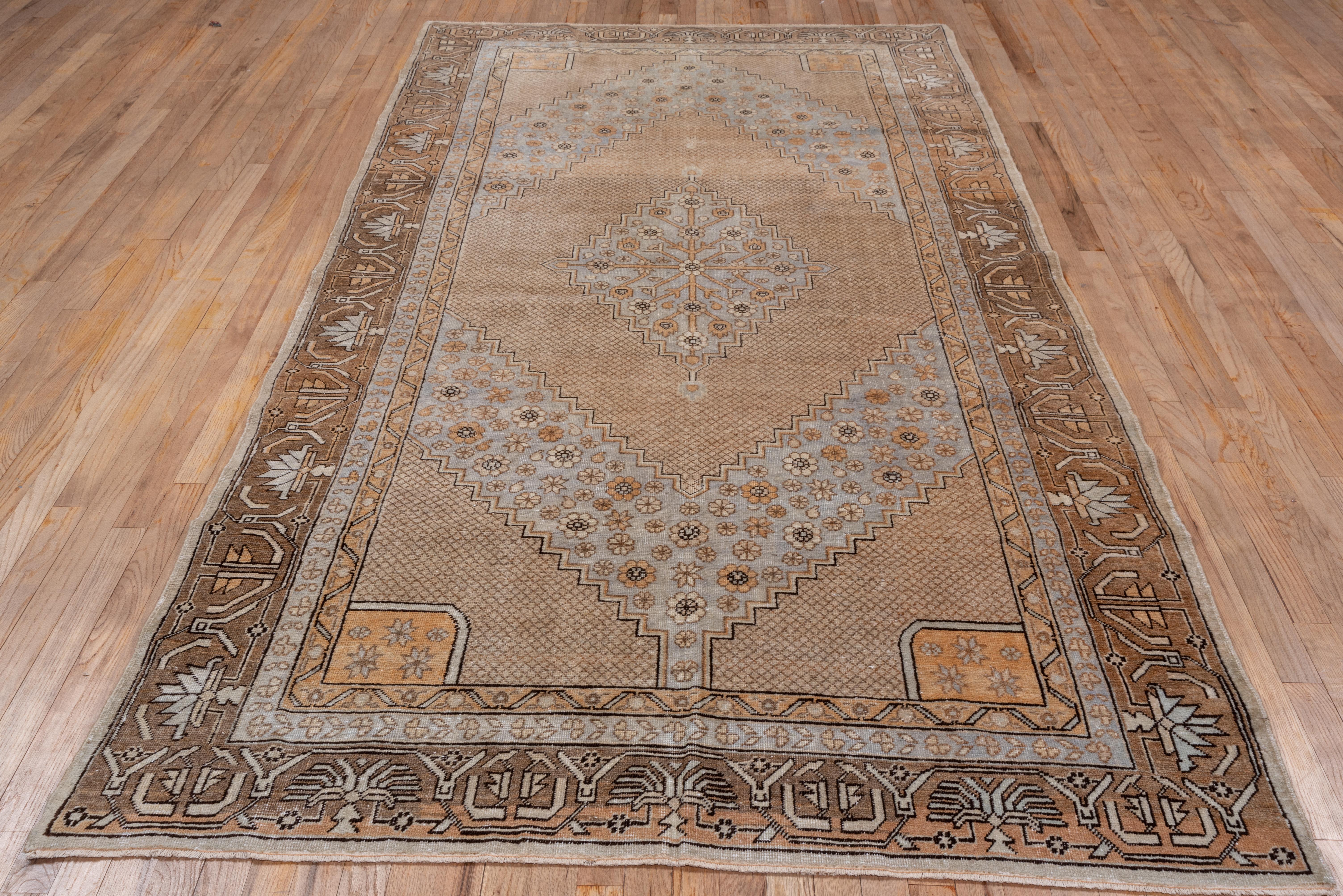 The corners are stepped in a small diamond lattice design, as is the subfield supporting a pale blue-grey stepped medallion enclosing a rosette trellis. Rosettes and botehs float freely on the pale blue-grey ground of this Xinjiang oasis town rug in