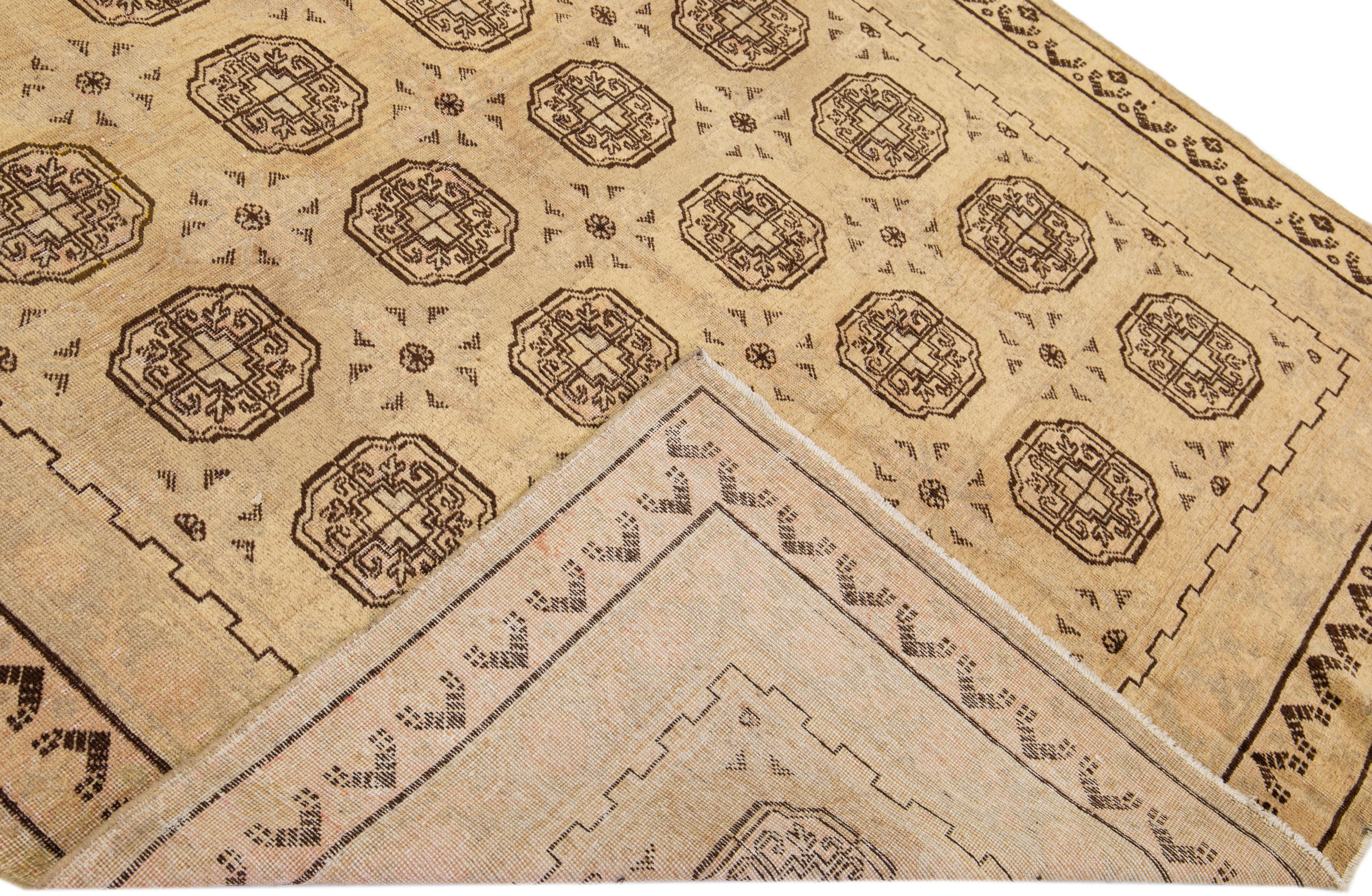 Magnifique tapis antique Khotan en laine nouée à la main avec un champ de couleur Tan. Ce tapis Khotan présente des accents marron, gris et pêche dans un design géométrique à médaillons multiples. 

Ce tapis mesure 6'5