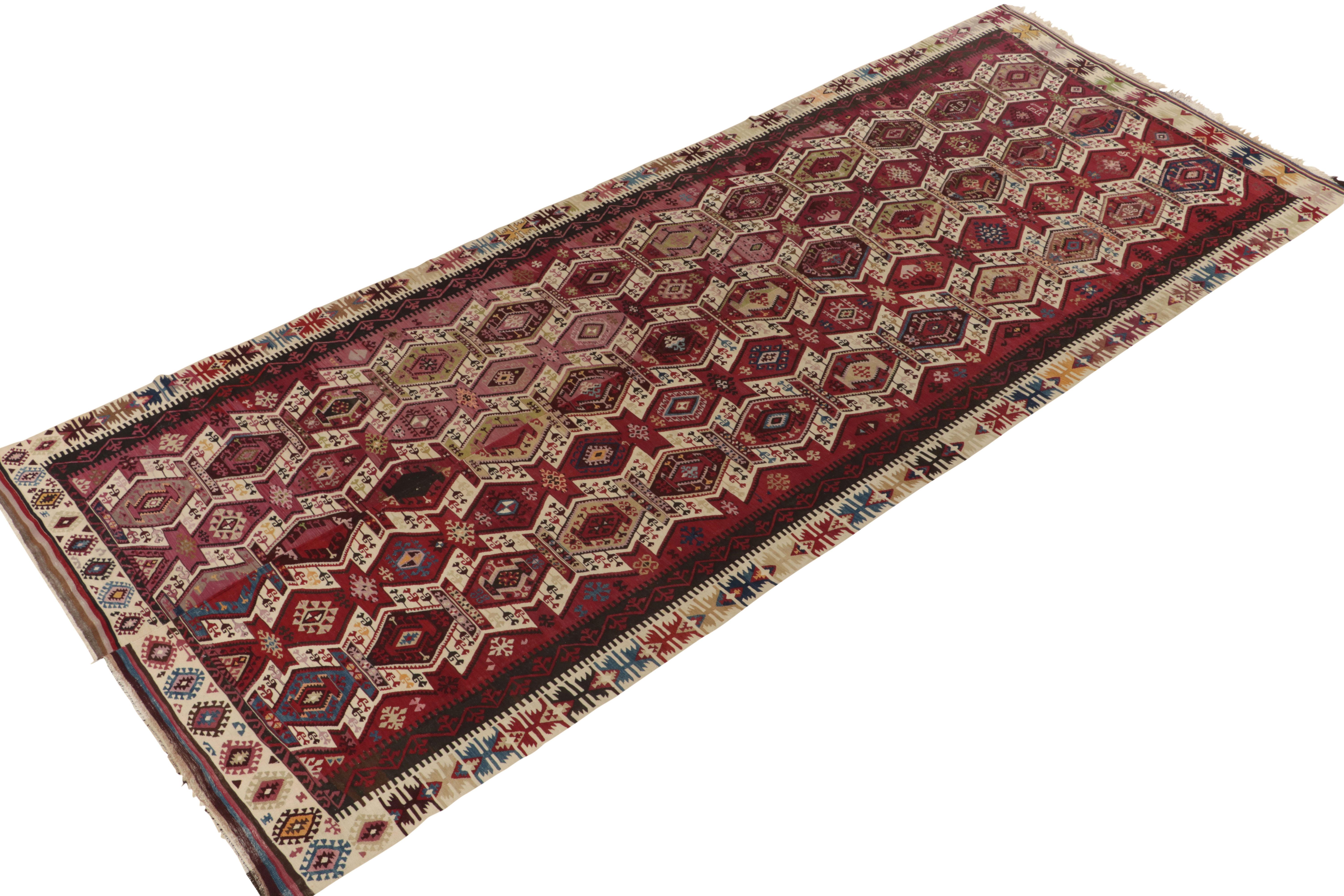 Connoting the celebrated tribal style, this 6x13 kilim rug hails from a special new curation of mid century flat weaves. This flatweave from Turkey enjoys a rare and desirable shade of red in the background. The wine-red hue with a lighter abrashed